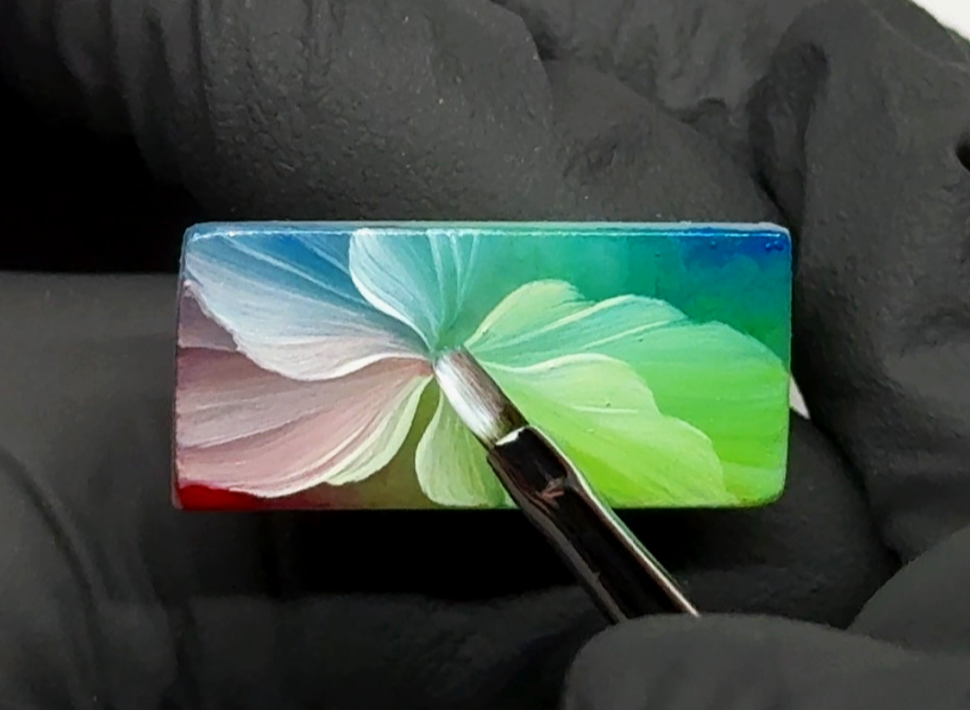 Flor camaleón artística pintada a mano sobre superficie cuadrada tamaño uña en tonos azul, verde fluorescente y blanco. Diseño de nail art profesional elaborado con técnica one stroke y gel painting para crear pétalos definidos, luminosos y con acaba