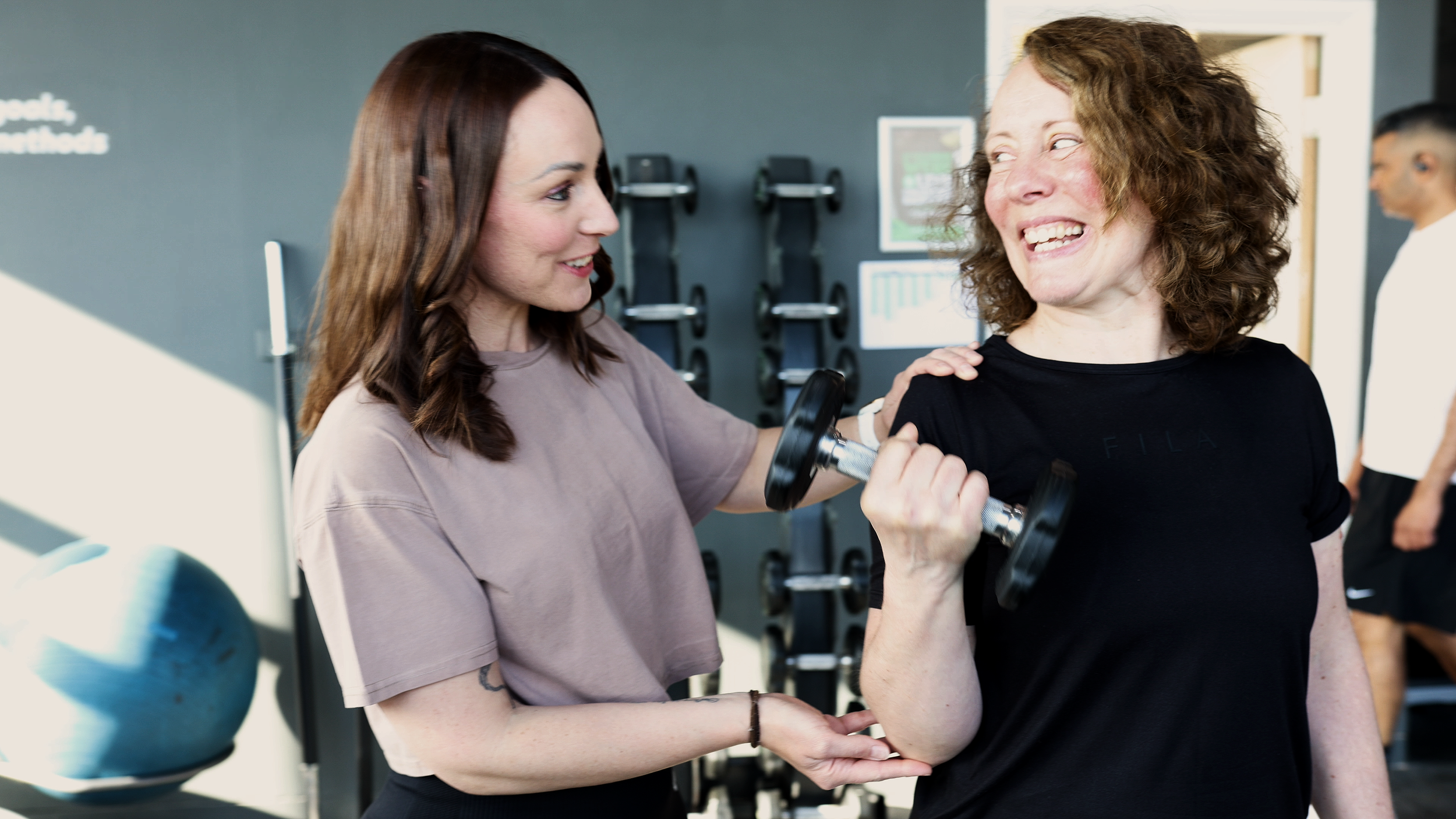 Candid lifestyle photography of personal trainer giving instruction to client holding a dumbbell for form.