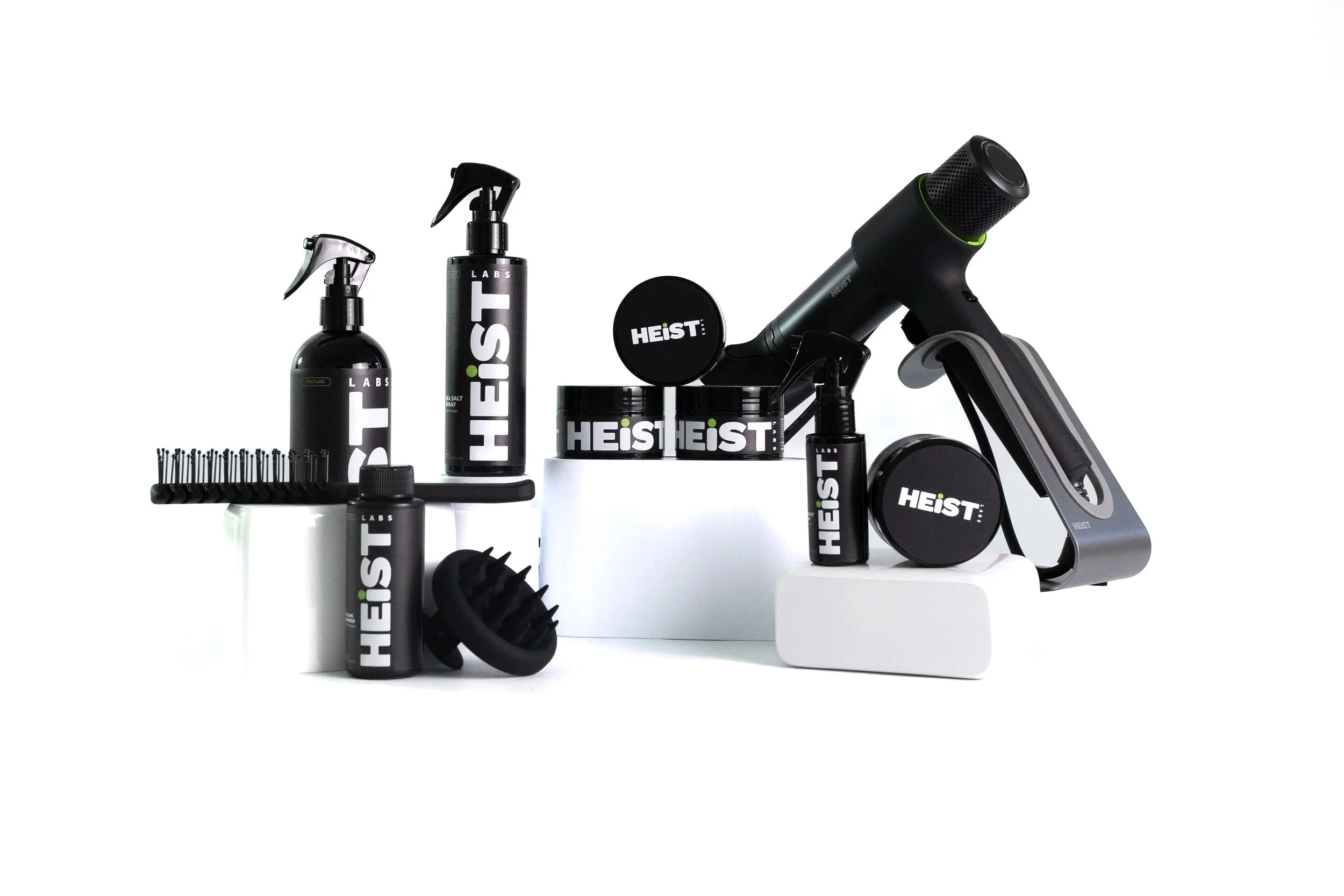 Collection of hair care and grooming products, including a hair dryer, sprays, gels, and brushes, all branded HEIST, arranged on a white background.