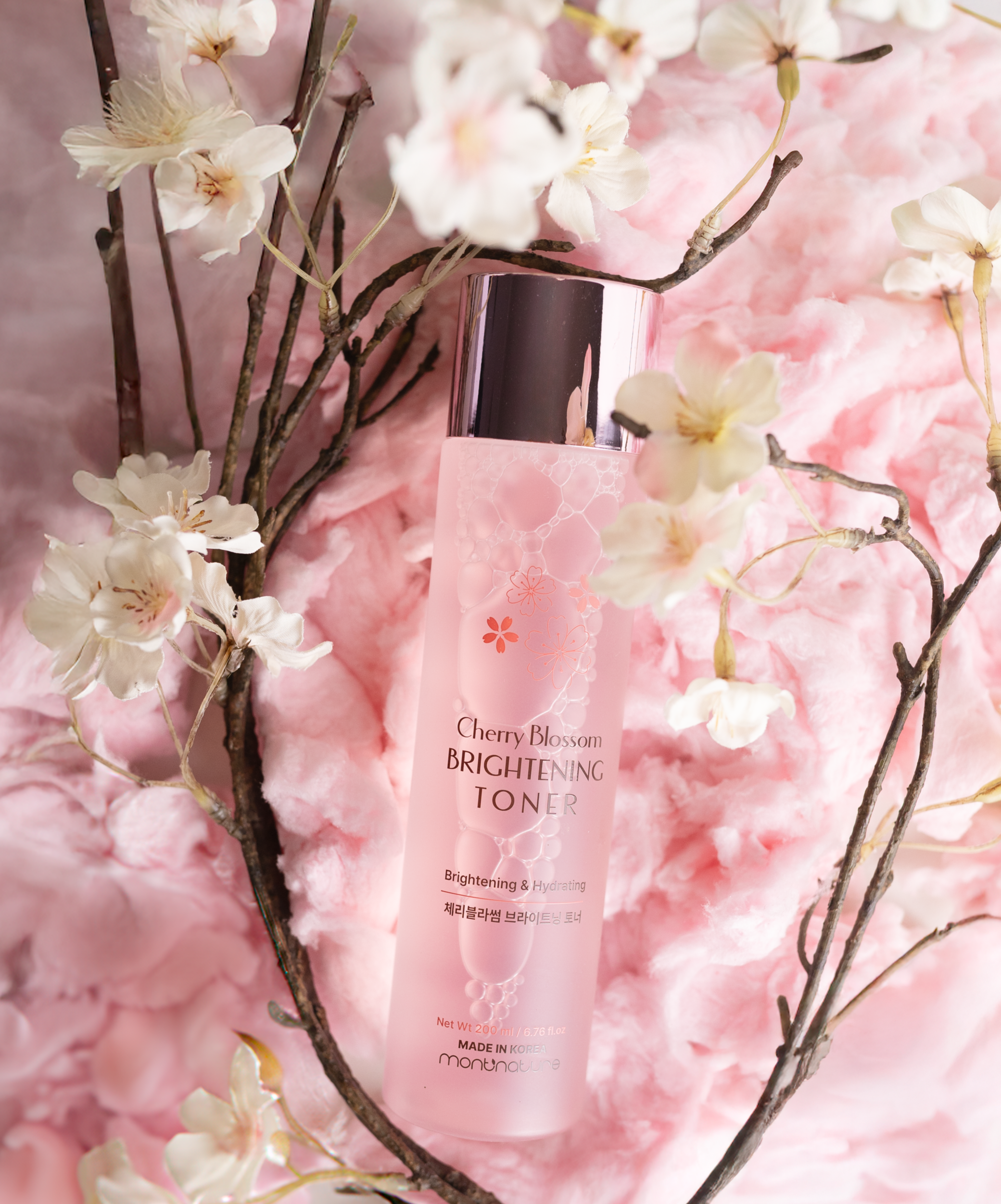 Pink bottle of Cherry Blossom Brightening Toner with cherry blossom branches and soft pink cotton candy background.