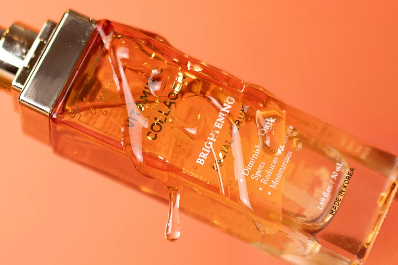 A clear glass bottle of Brigid's Algae Facial Oil with water droplets on it, lying on its side on an orange background.