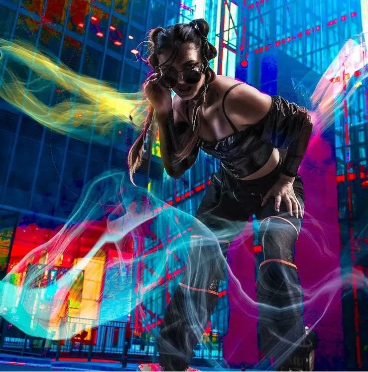 A woman with black hair styled in buns, wearing sunglasses, a black top, and pants, stands in front of brightly colored neon lights and dynamic light effects in an urban setting at night.