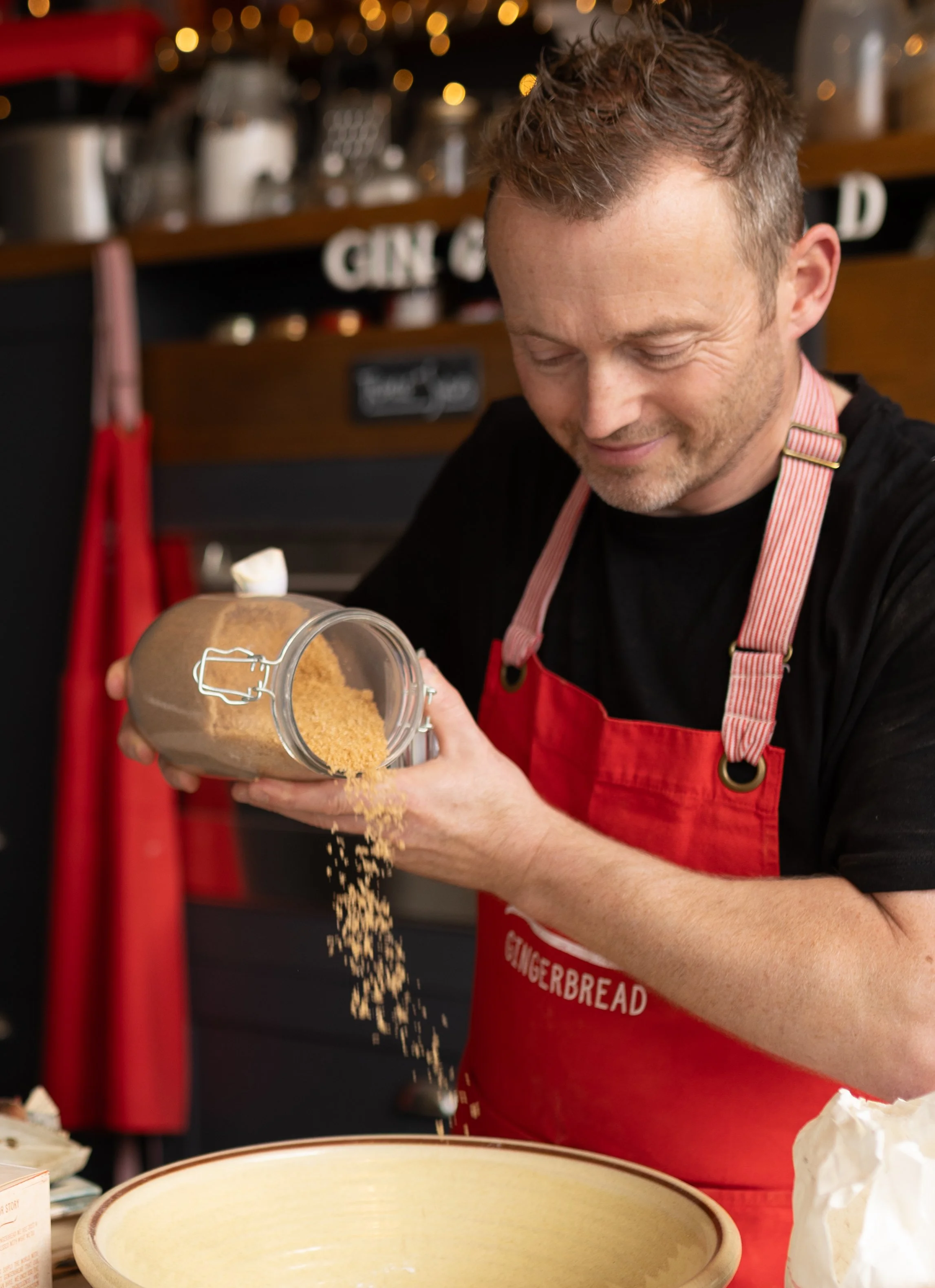 Candid brand photography of artisan baker pouring brown sugar from jar for product ingredients.