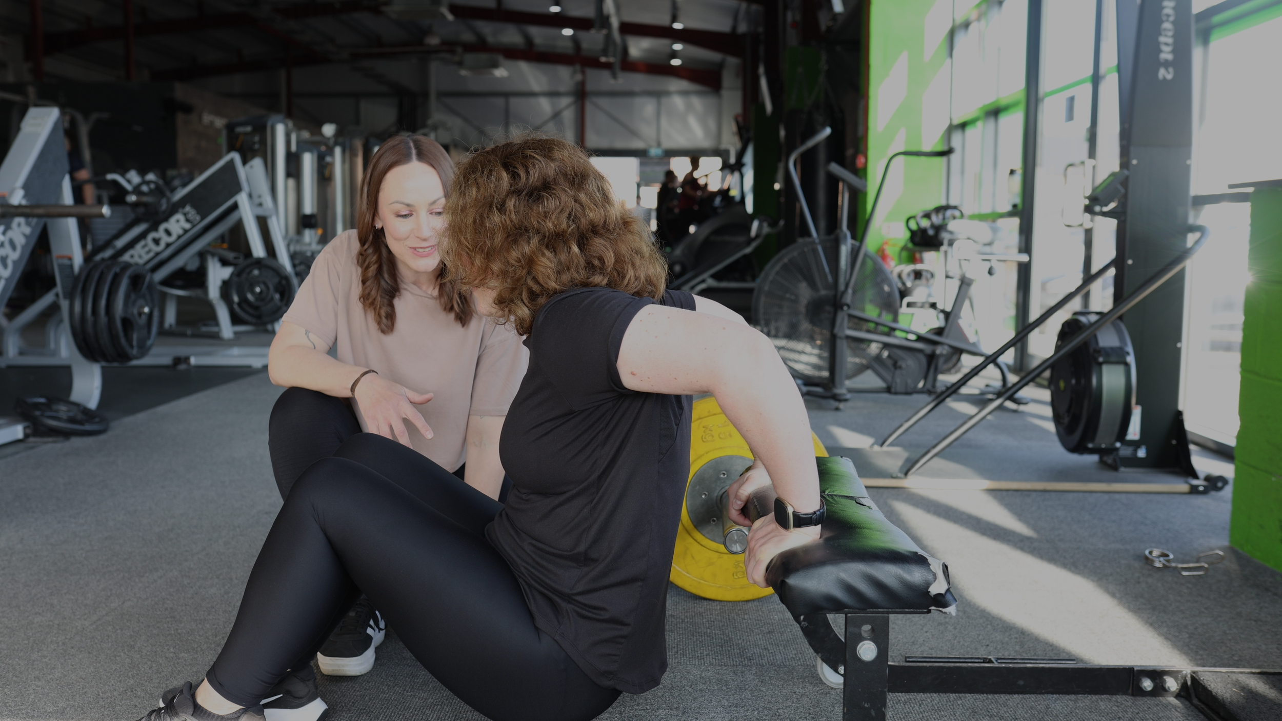 Dynamic gym photography of personal trainer helping client adjust form on a weight workout bench.