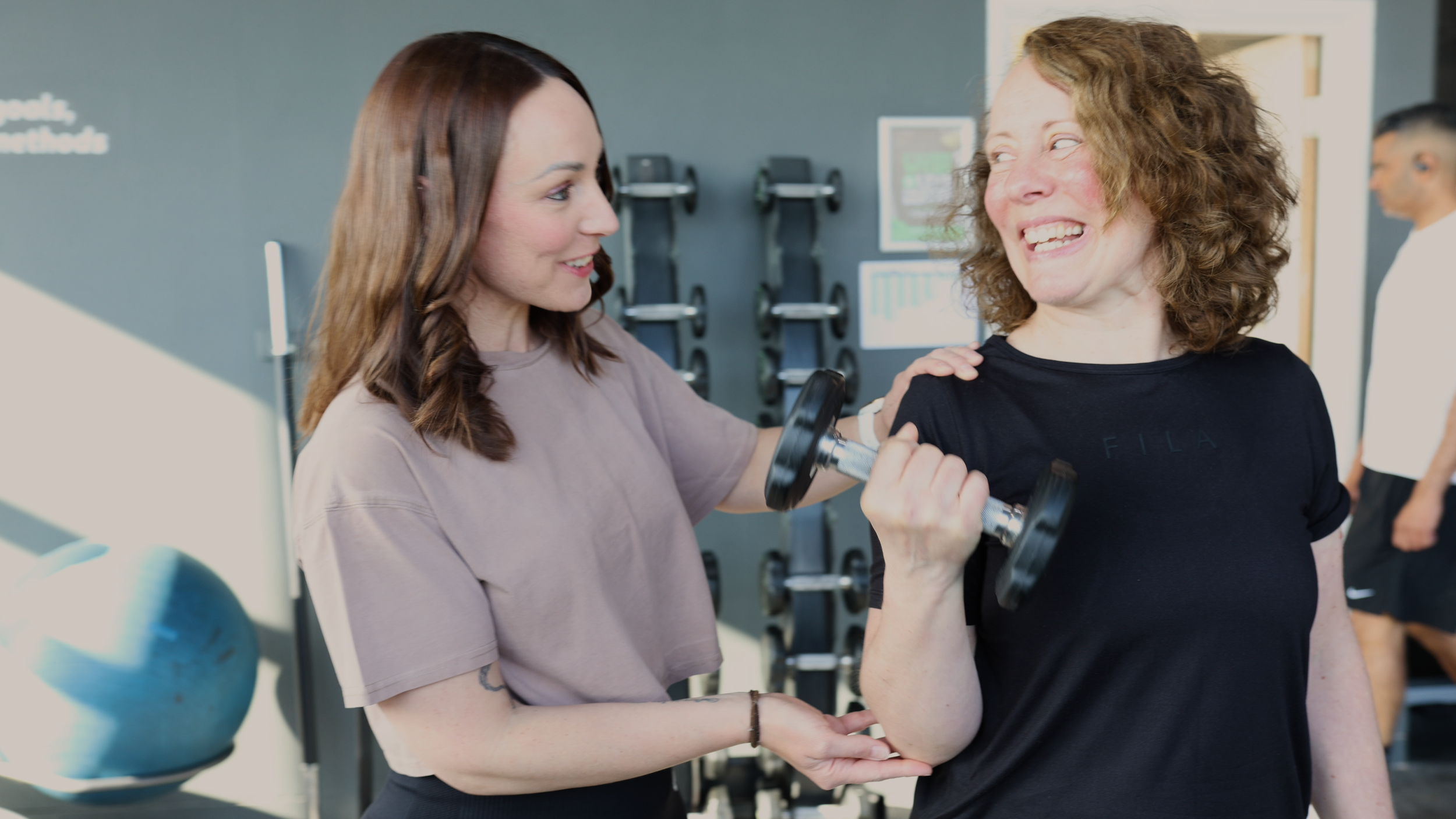 Candid lifestyle photography of personal trainer giving instruction to client holding a dumbbell for form.