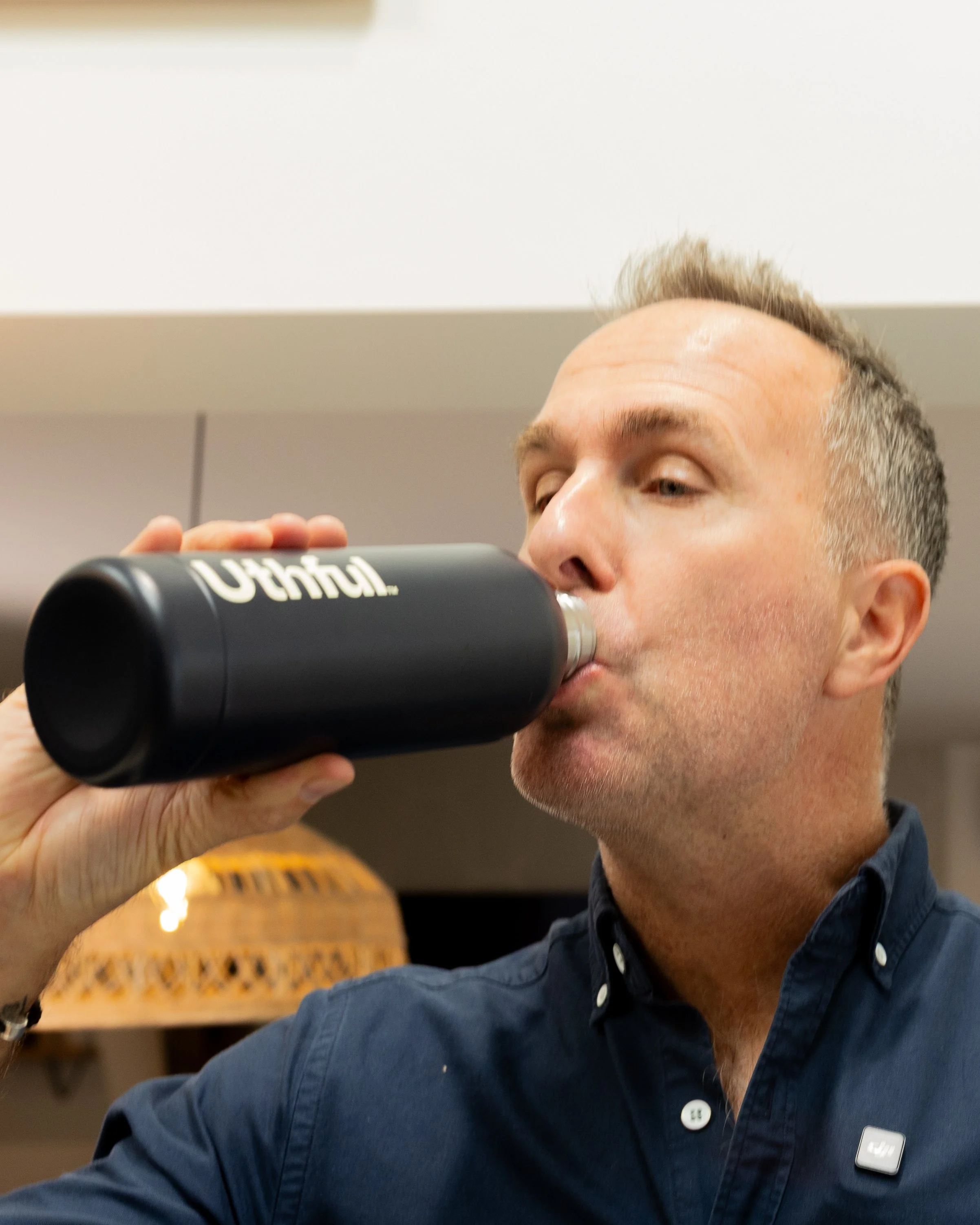 A man drinking from a black thermos in an indoor setting.