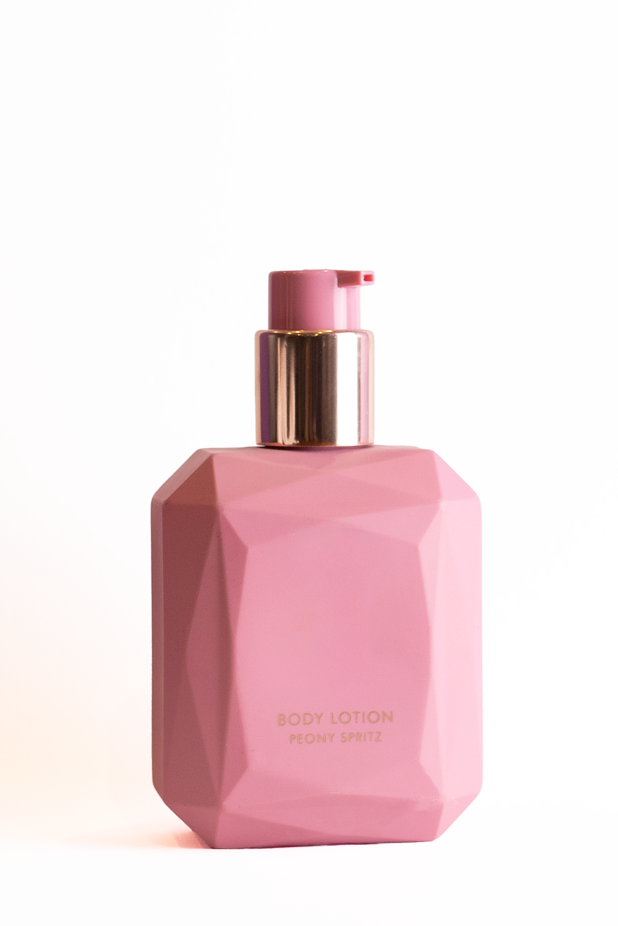 Pink geometric-shaped body lotion bottle with gold accents, labeled 'Body Lotion Peony Spritz'.