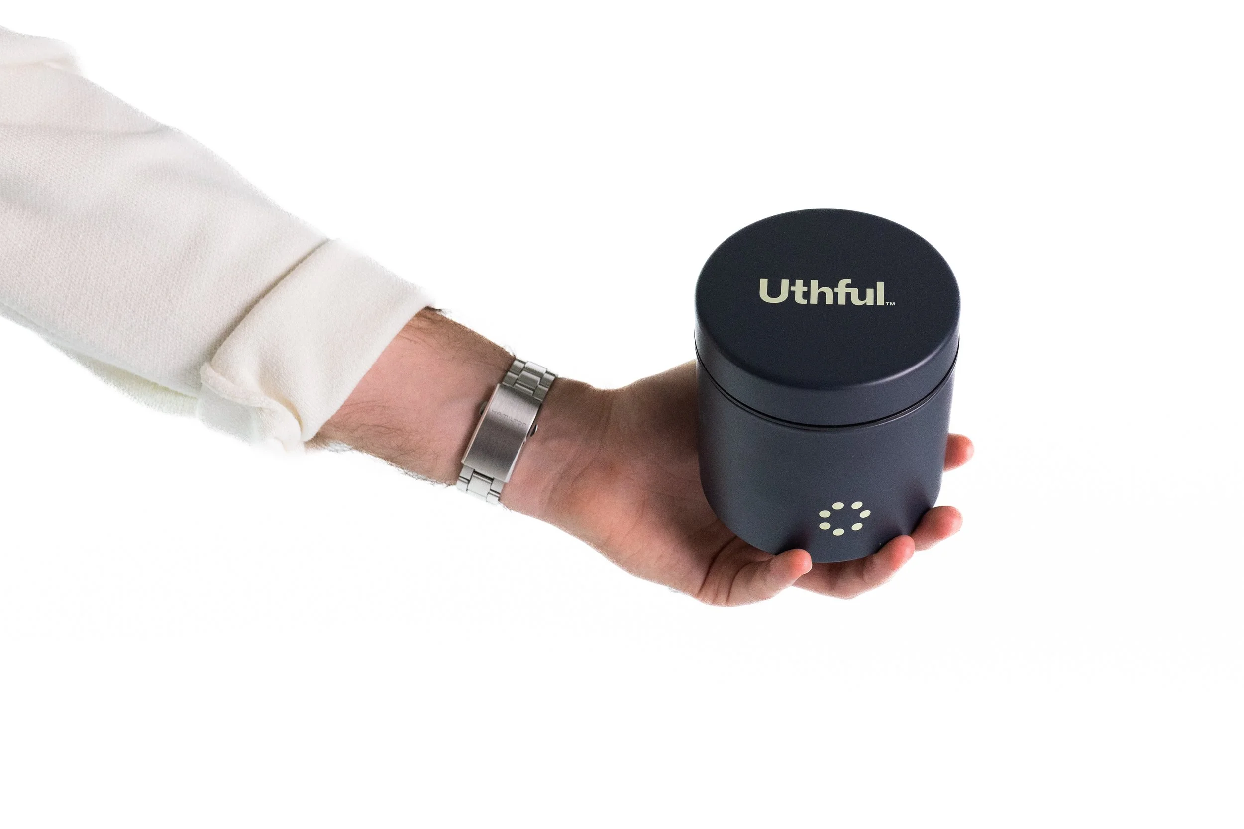 A person holding a black cylindrical object with the brand name Uthful on top, wearing a white long-sleeve shirt and a silver wristwatch against a white background.