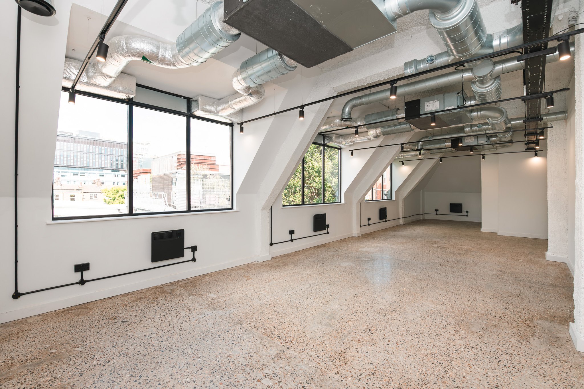 Empty commercial office space with large windows, exposed ductwork, and terrazzo flooring.