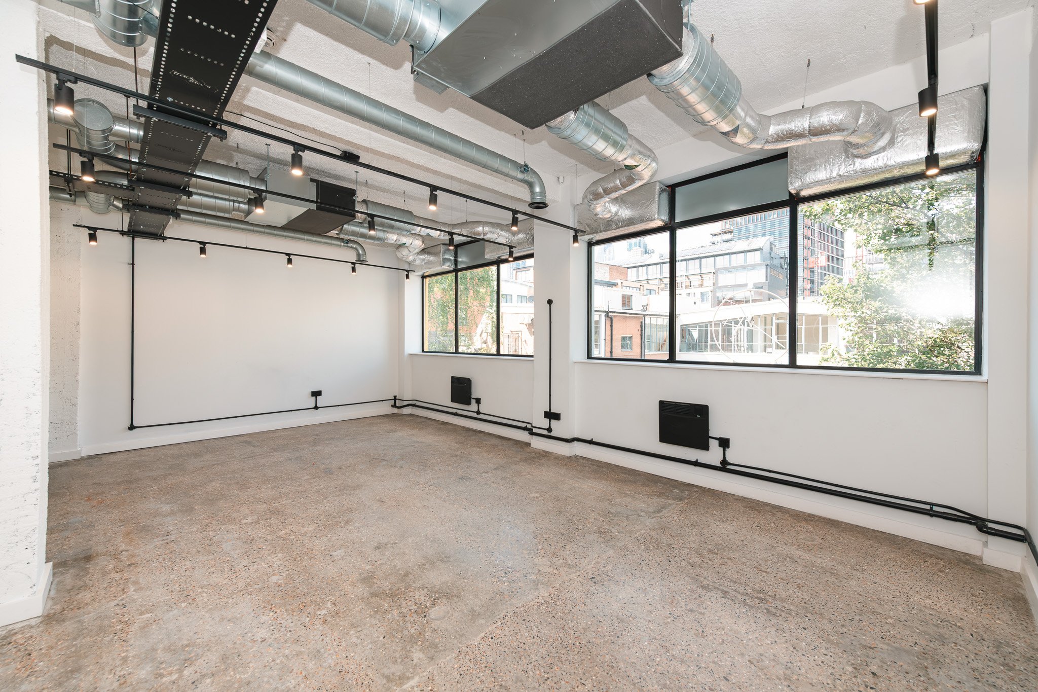 Empty modern industrial-style room with large windows, exposed ductwork on ceiling, and electrical wiring along walls.