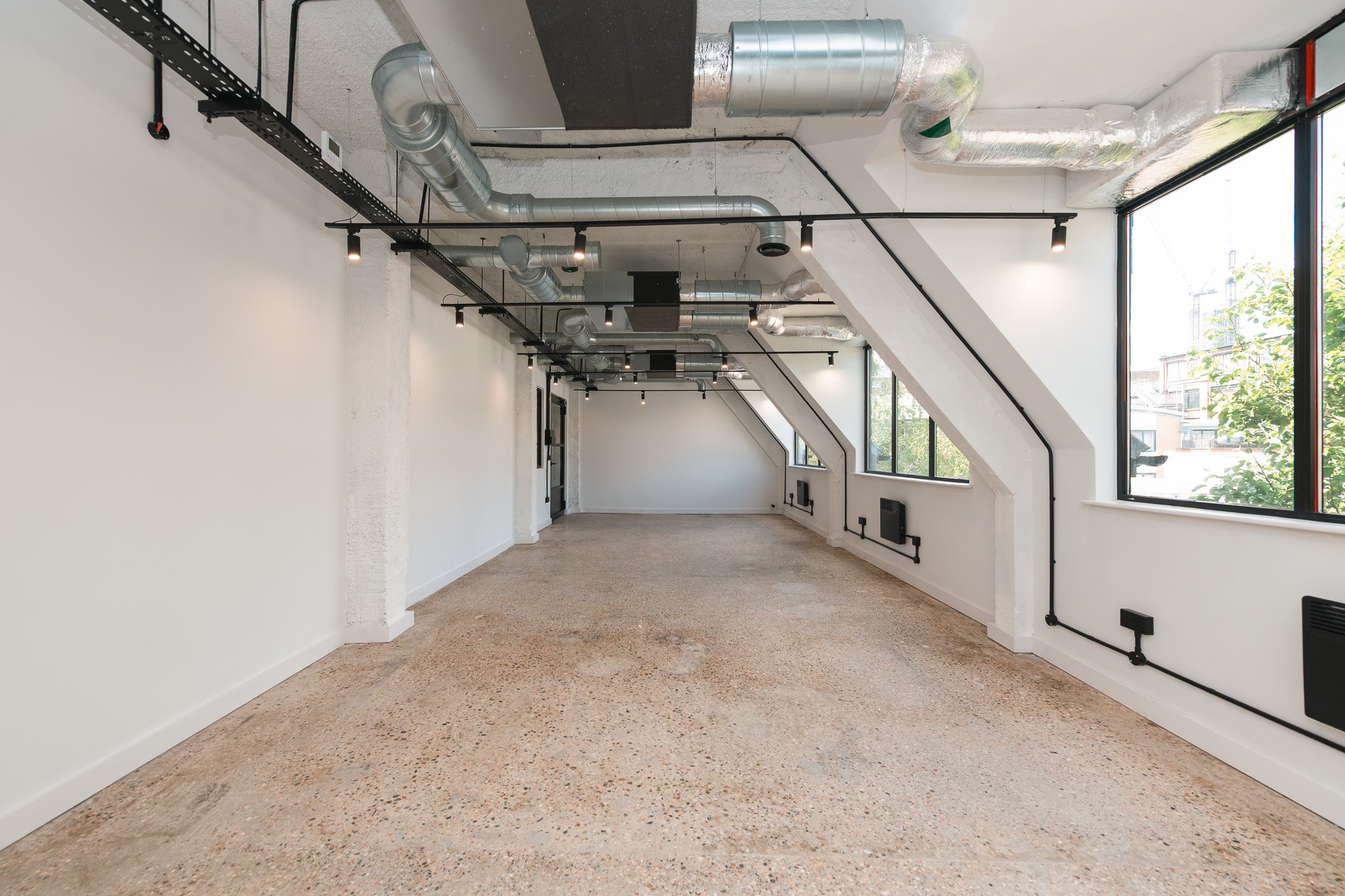 Empty room with white walls, large windows, exposed ductwork on ceiling, and a polished concrete floor.