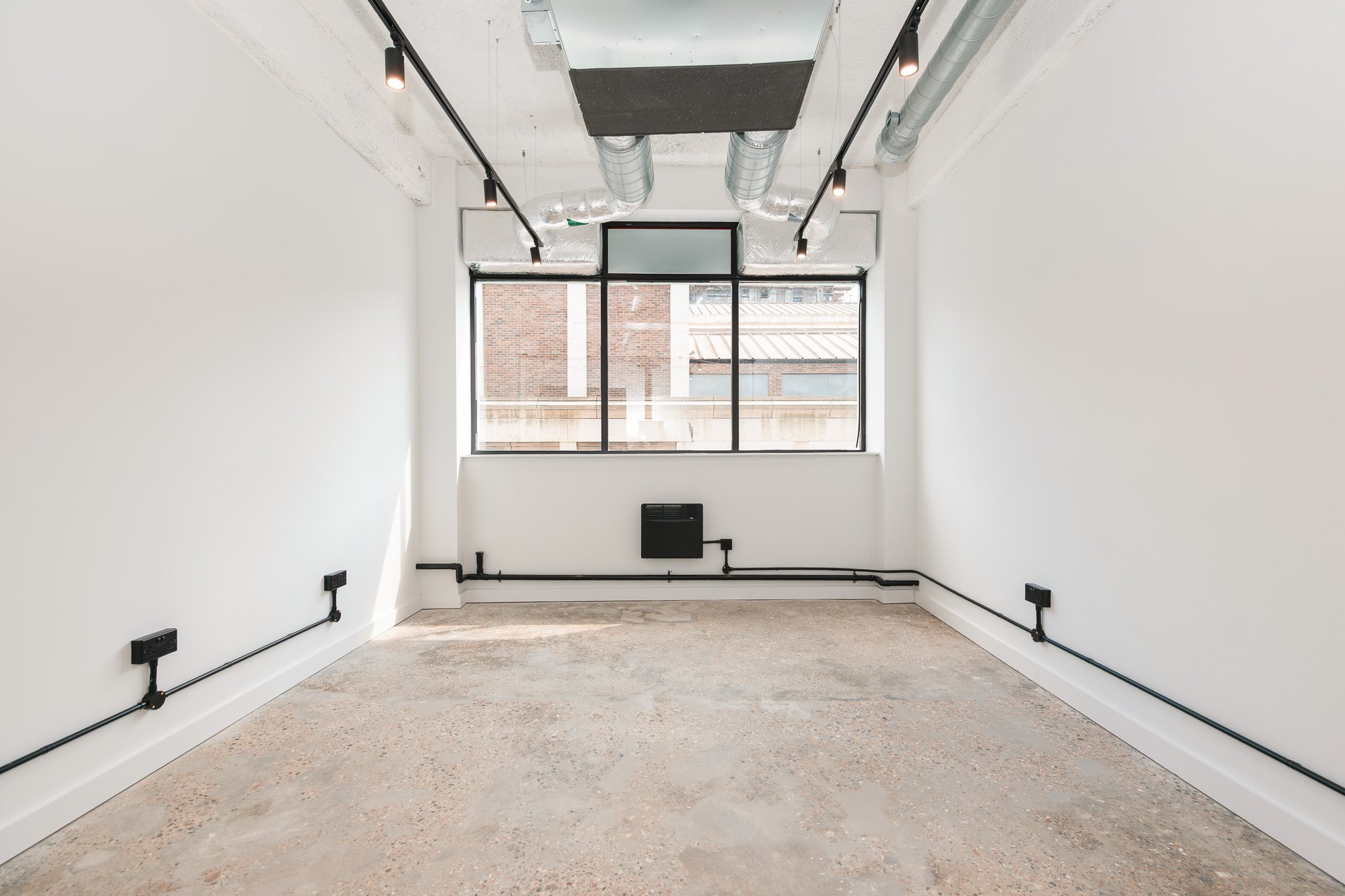 Empty room with white walls, large window, exposed ductwork, and electrical outlets along the baseboards.