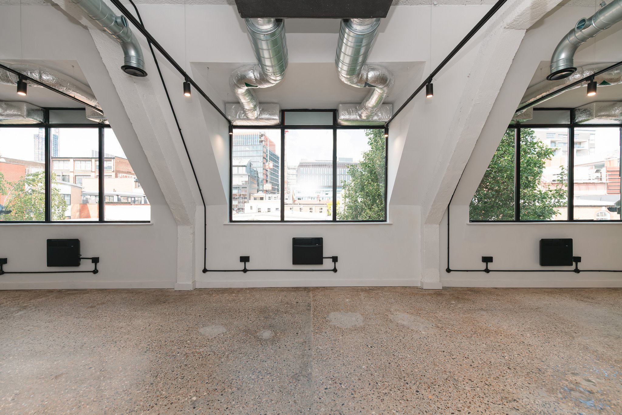 Empty modern office space with large windows, exposed ductwork, and a speckled floor.