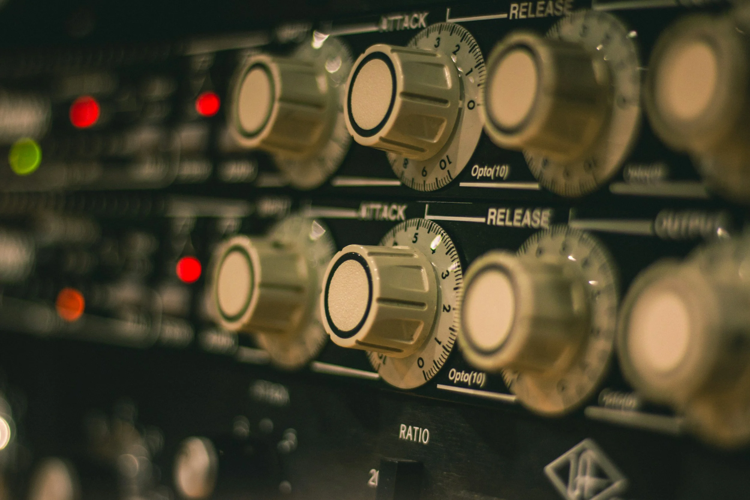 Close-up of audio equipment with several beige control knobs, indicating functions like attack and release, with small red and green indicator lights in the background.