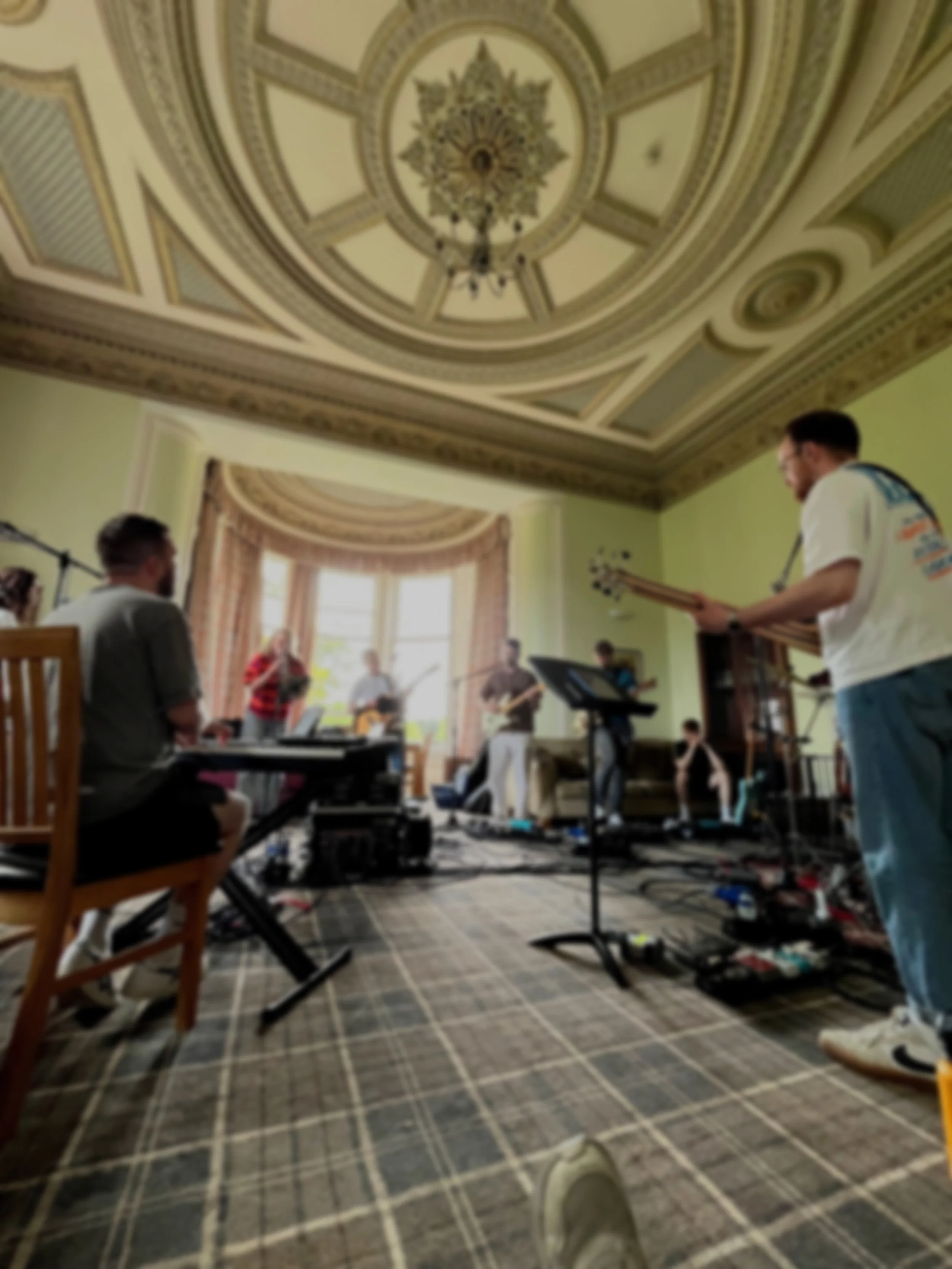 A group of musicians performing in a grand, ornate room with high ceilings, chandelier, and large windows.