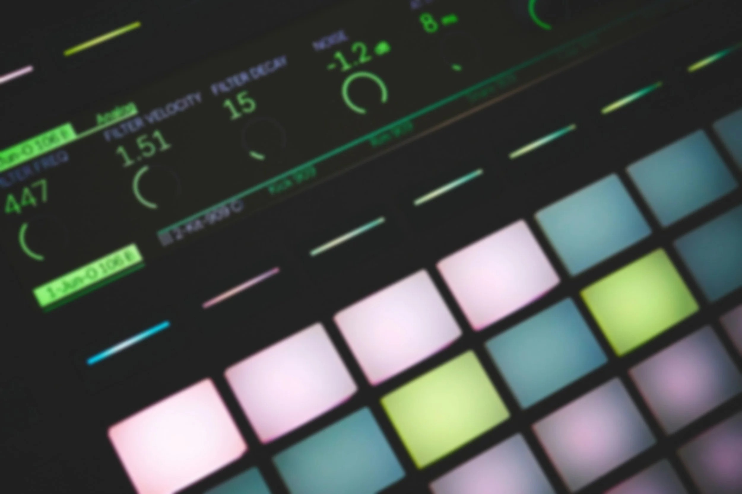 Close-up of an electronic music controller with colorful pads and knobs, displaying green, pink, and blue lights.