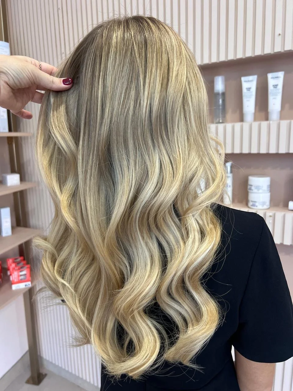 Back of a woman's head showing long, wavy blonde hair in a salon setting.