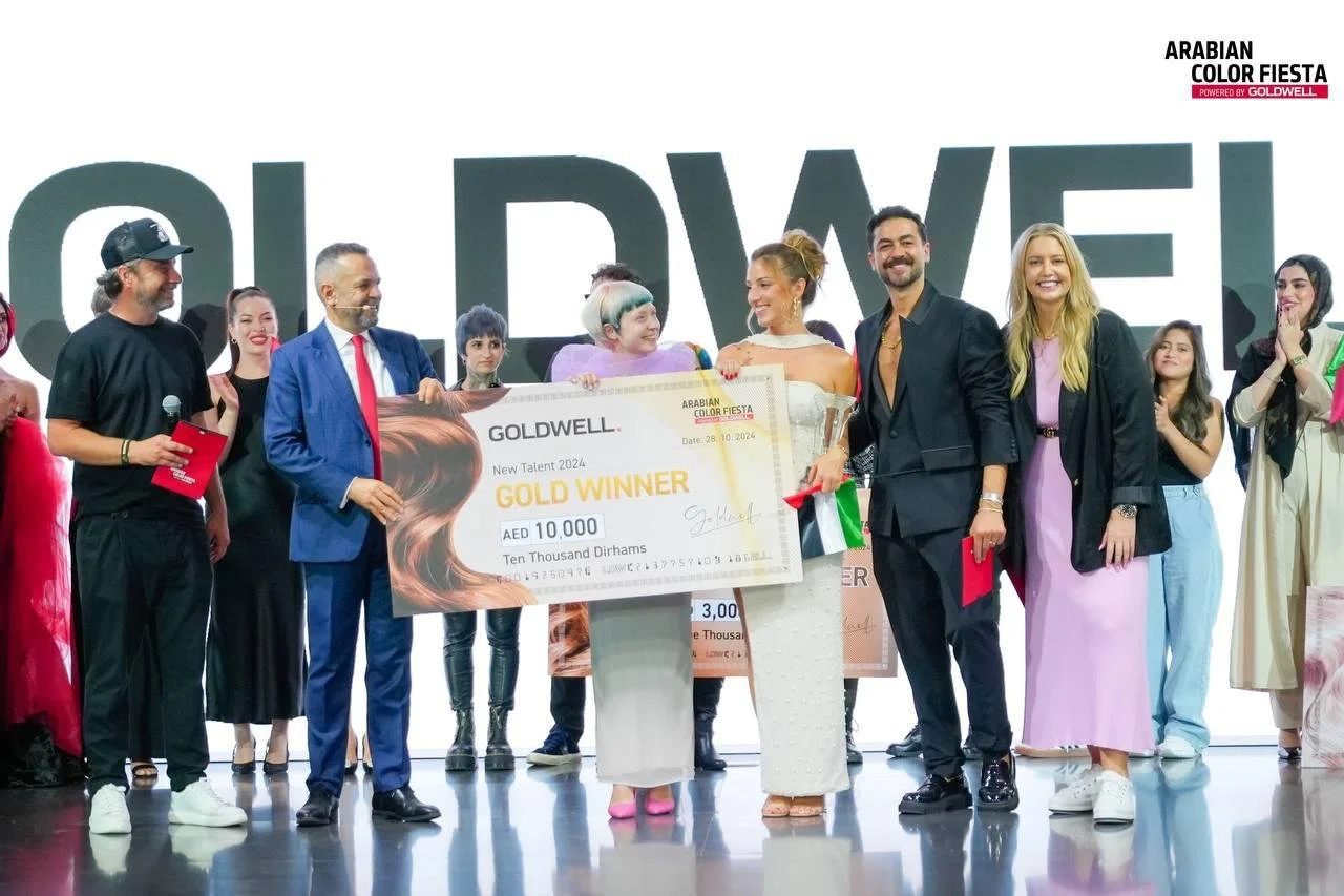 Group of people on stage celebrating, holding a large symbolic cheque for AED 10,000 as gold winner at an event titled 'Arabian Color Fiesta.'