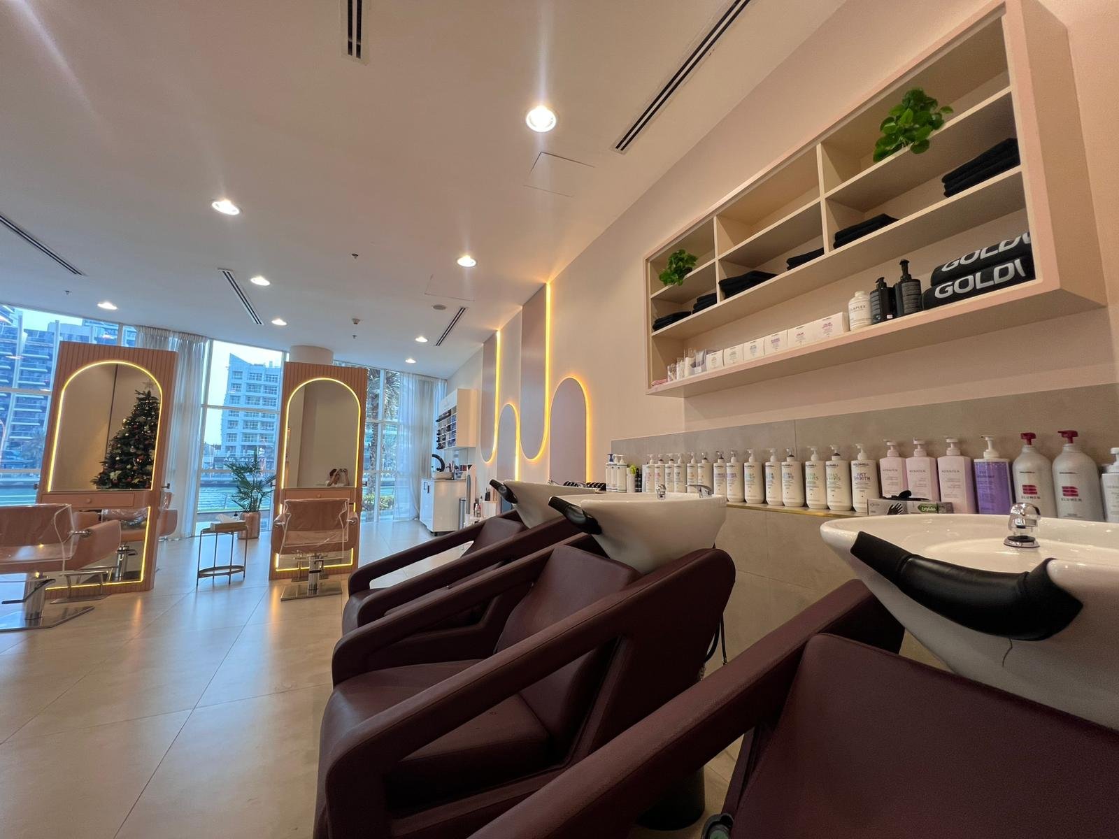 Interior of a modern hair salon or spa with washing stations, salon chairs, large windows, and a Christmas tree in the background.