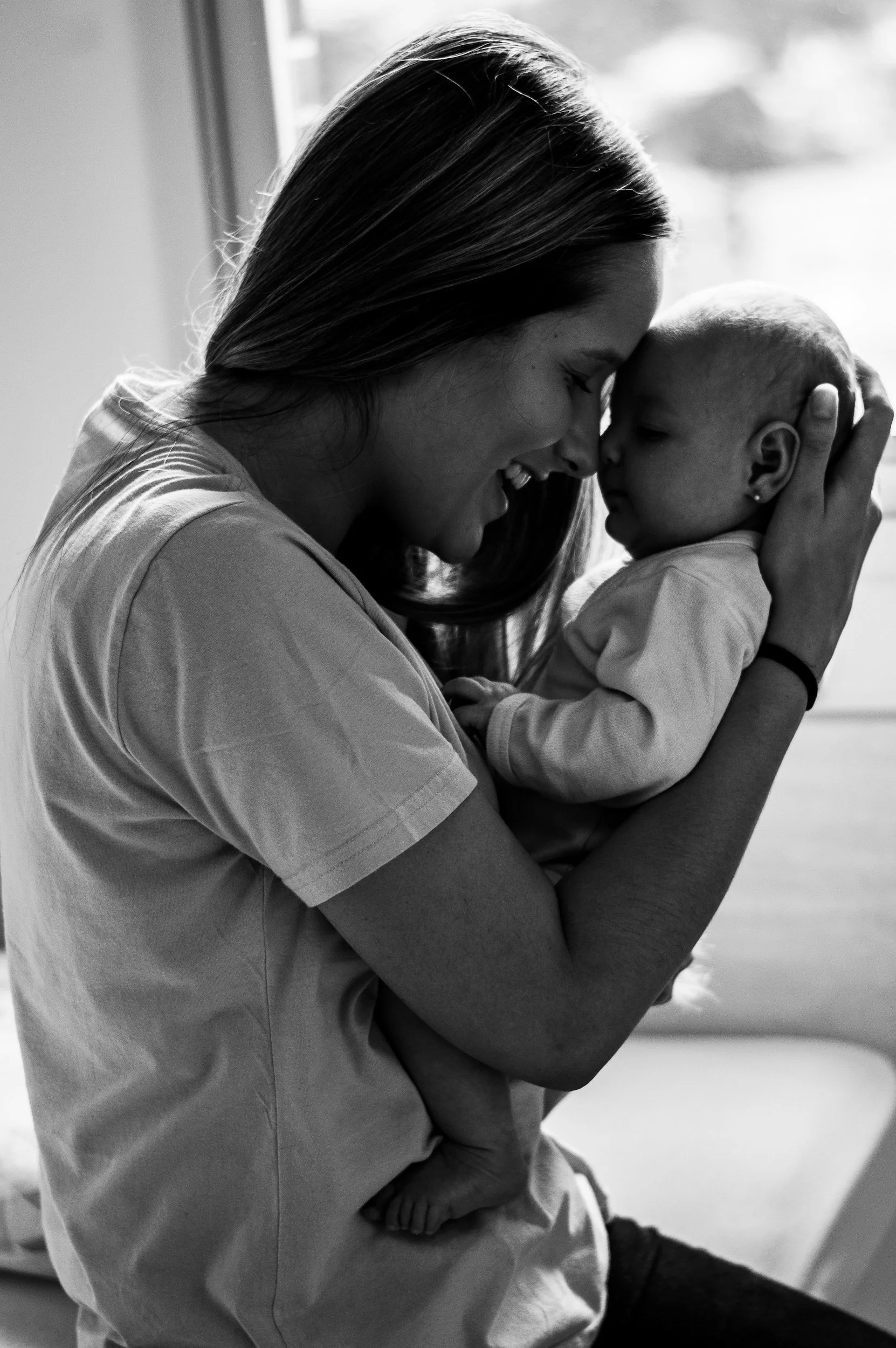 A woman holding a small child close to her face, with their foreheads touching, sharing a joyful moment indoors.