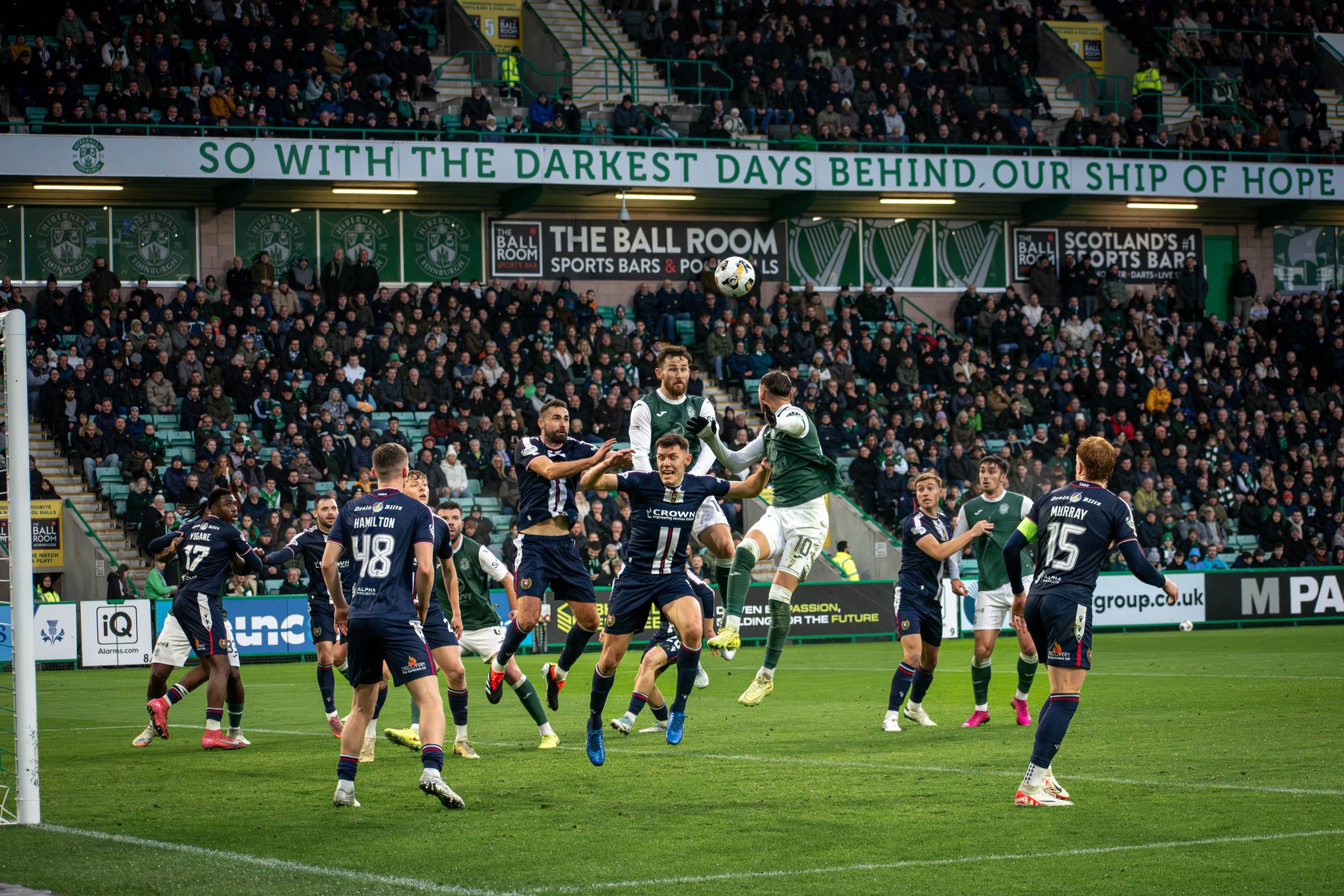 Soccer players in action during a match, with fans watching in a stadium filled with banners and advertisements.