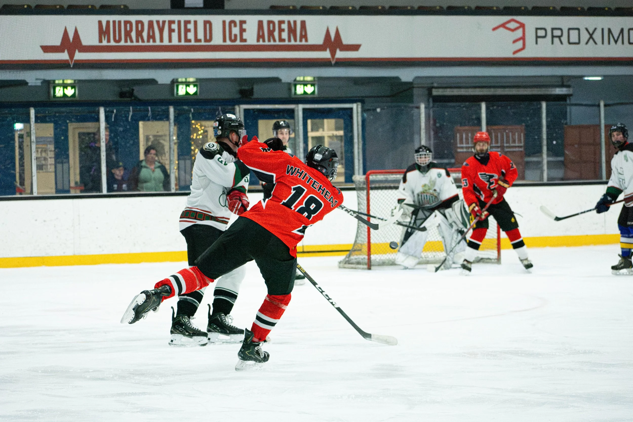 Hockey players competing on ice rink during a game at Murrayfield Ice Arena, with spectators in the background.