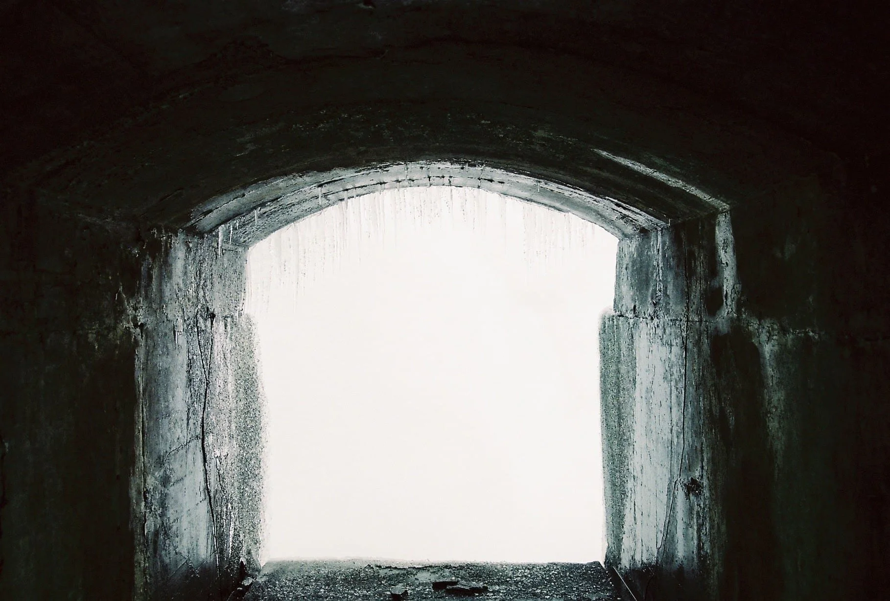 Dark tunnel opening to bright light outside, with concrete walls showing cracks and discoloration.