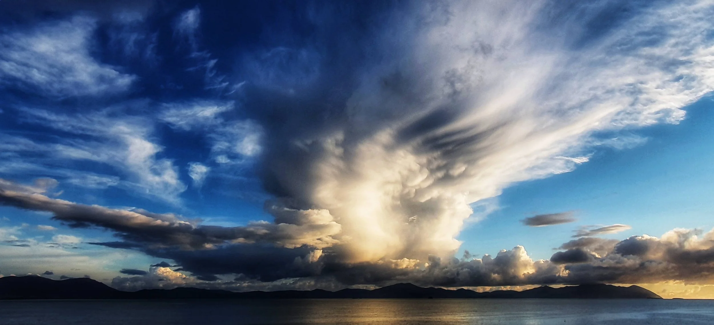 A dramatic sky filled with clouds over a calm body of water with distant mountains.