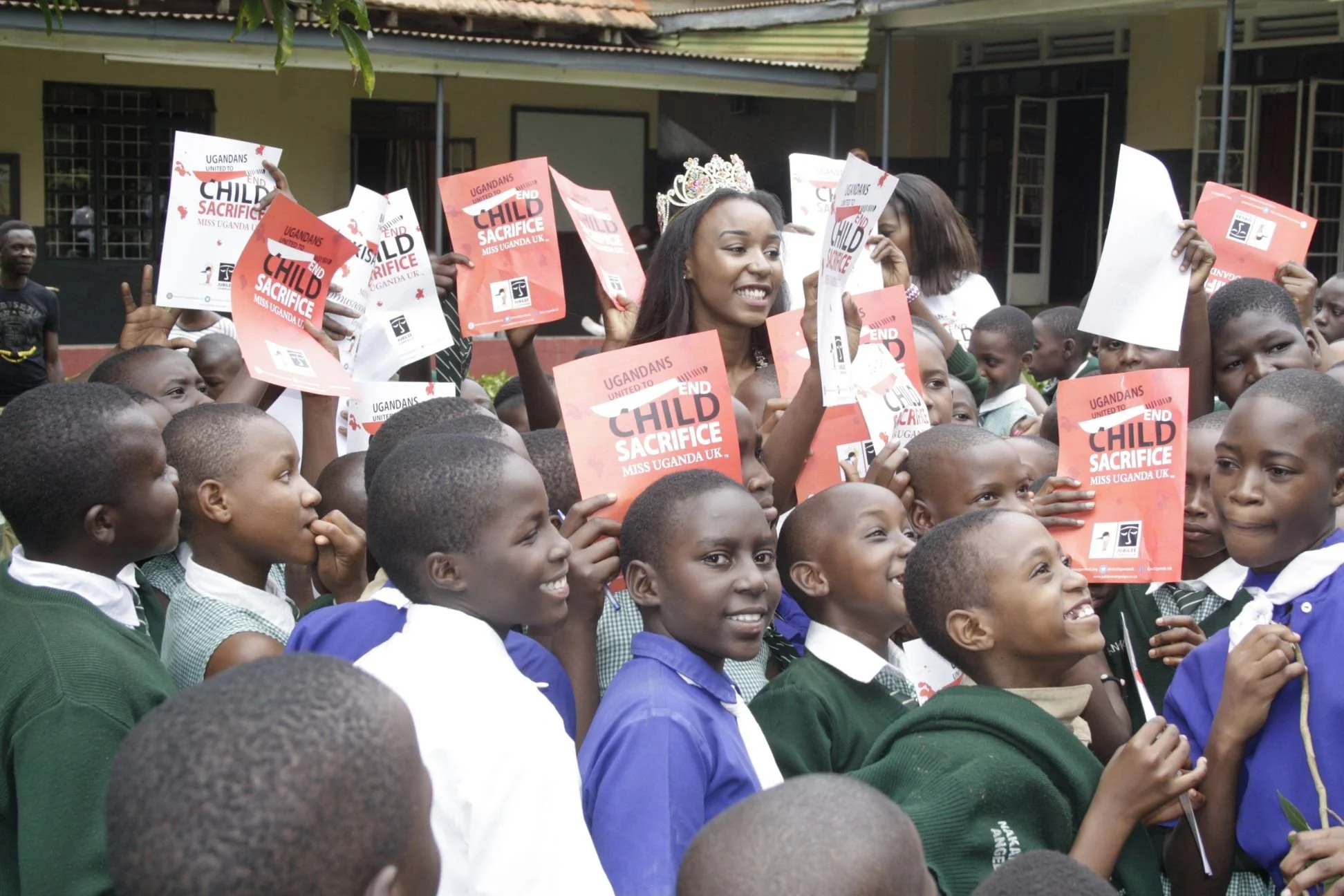 Group of children holding up placards that say 'End Child Sacrifice' during a rally or awareness event, with a woman wearing a crown among them.