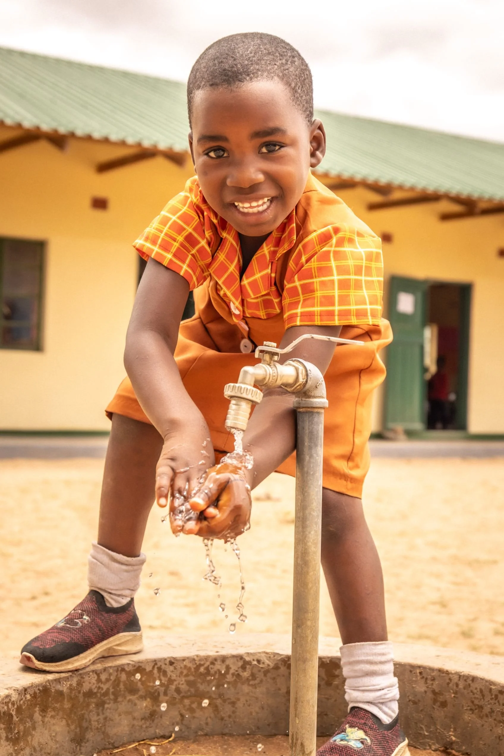 Happy child getting clean water from a tap outside Jessie's House
