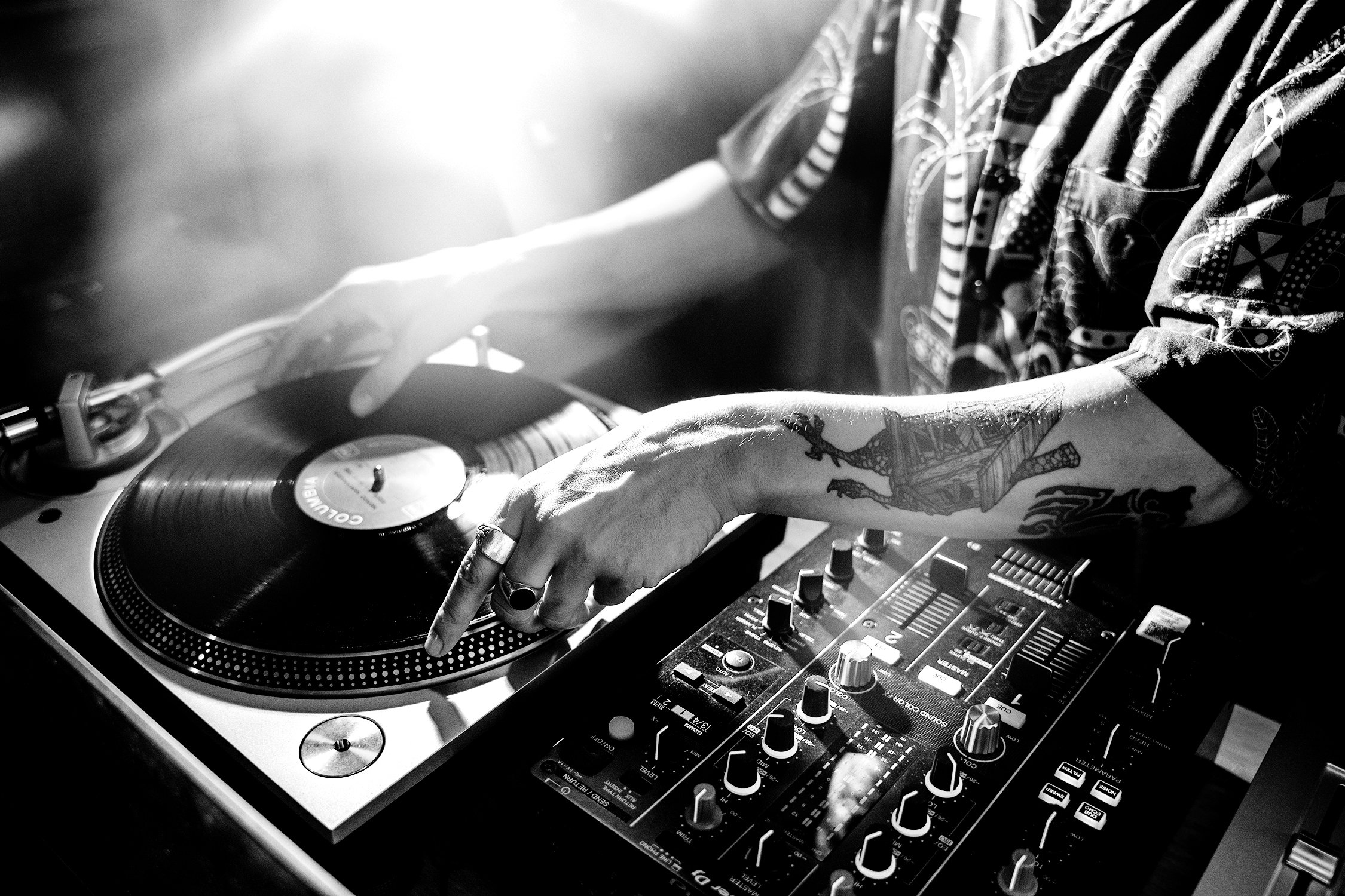 Close-up of a DJ's hands operating a turntable and mixer during a performance, black and white photograph. Event photographer in Barcelona.