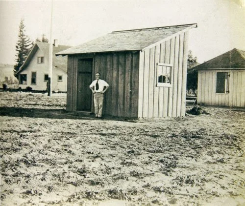A black and white photo of a young man in front of a small building in Los Angeles