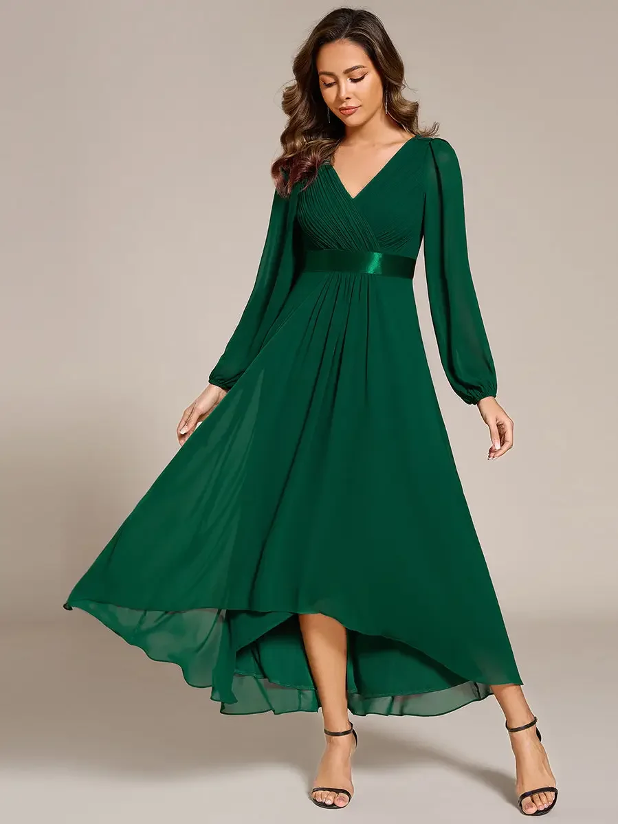 A woman in a long, emerald green dress with a V-neck and long sleeves, standing with one foot slightly forward and looking down.