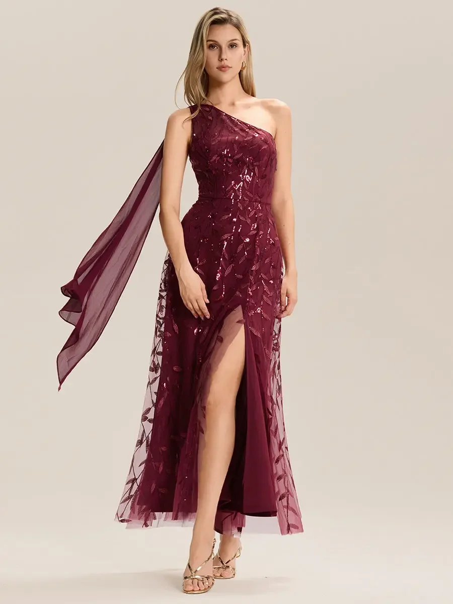 A woman wearing a burgundy, one-shoulder evening gown with a high slit, standing against a plain background.