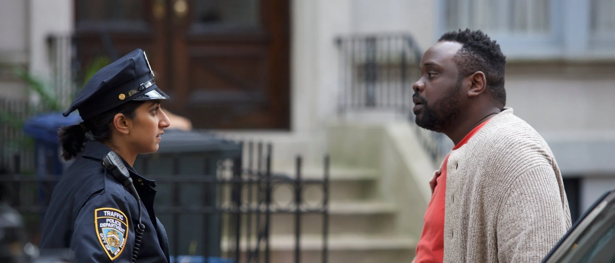 A woman police officer and a man stand face to face on a city sidewalk, engaging in conversation.