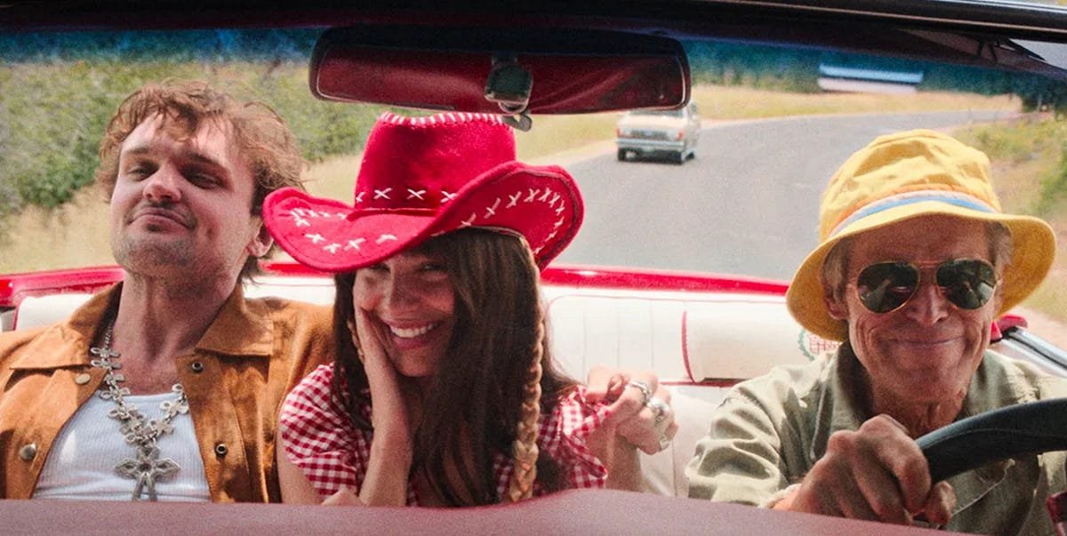 Three people in a car with two men and a woman in the backseat, wearing colorful hats, smiling and enjoying a road trip.