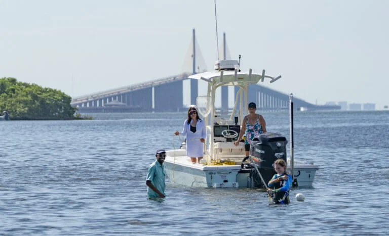 Four people on and around a boat in the water with a bridge in the background.