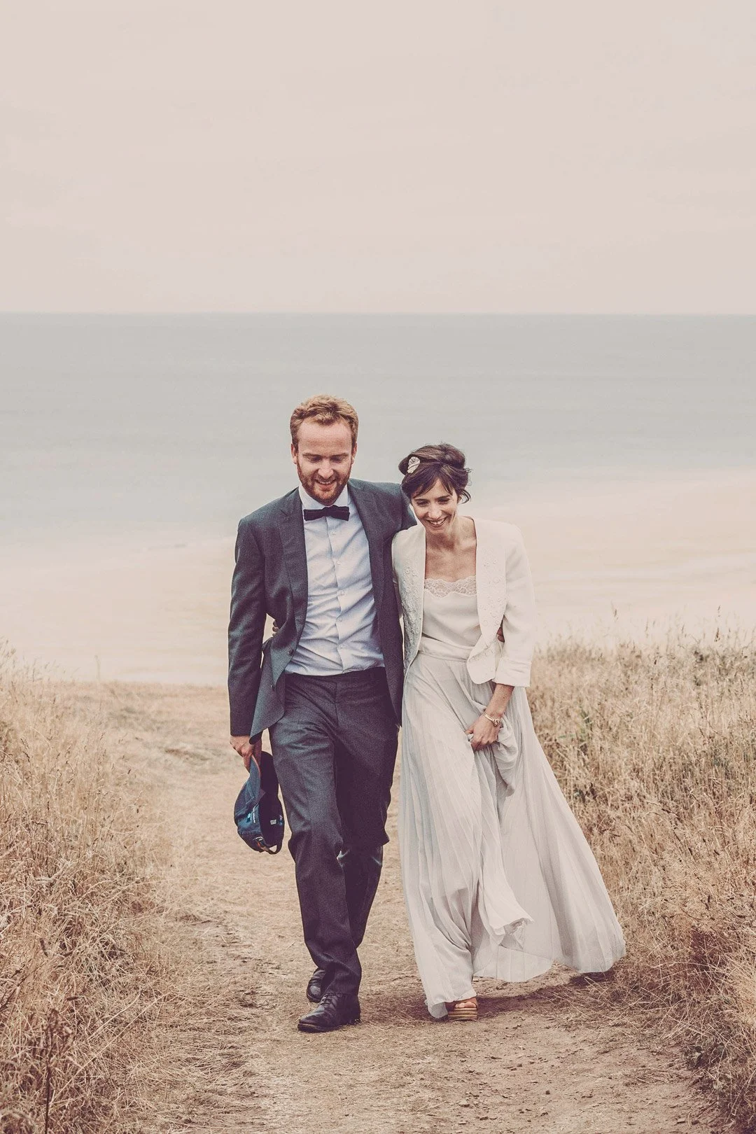 Séance photo de couple en extérieur, mariés marchant main dans la main au bord de la mer