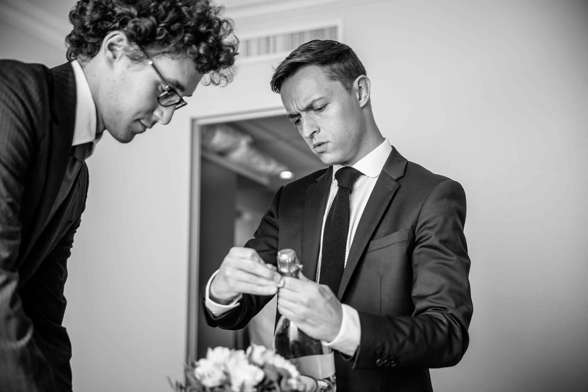 Deux jeunes hommes ouvrent une bouteille de champagne lors des préparatifs des mariés.