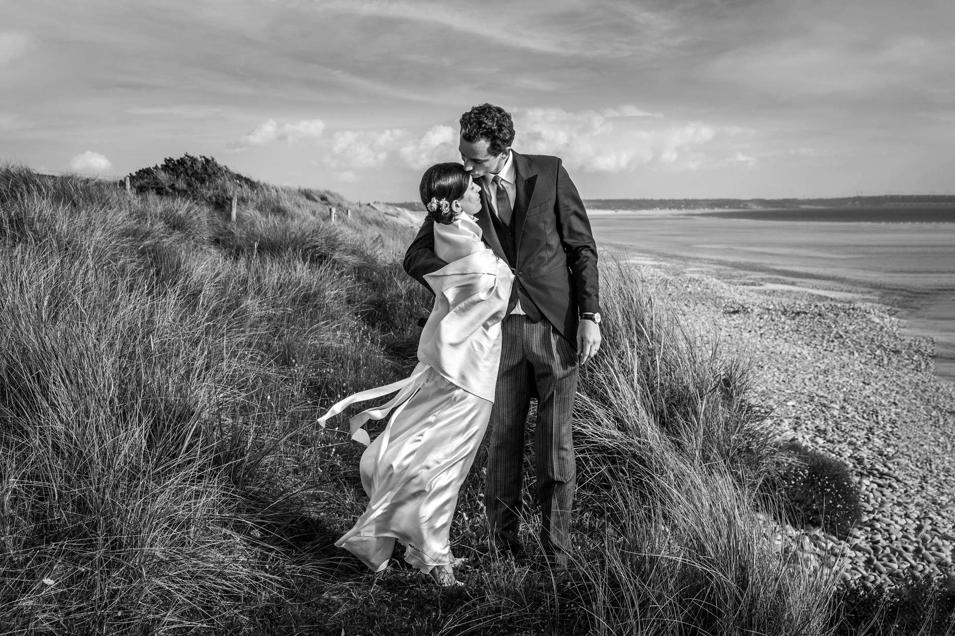 Un couple en vêtements de mariage sur une plage, l'homme tiens une femme dans ses bras.