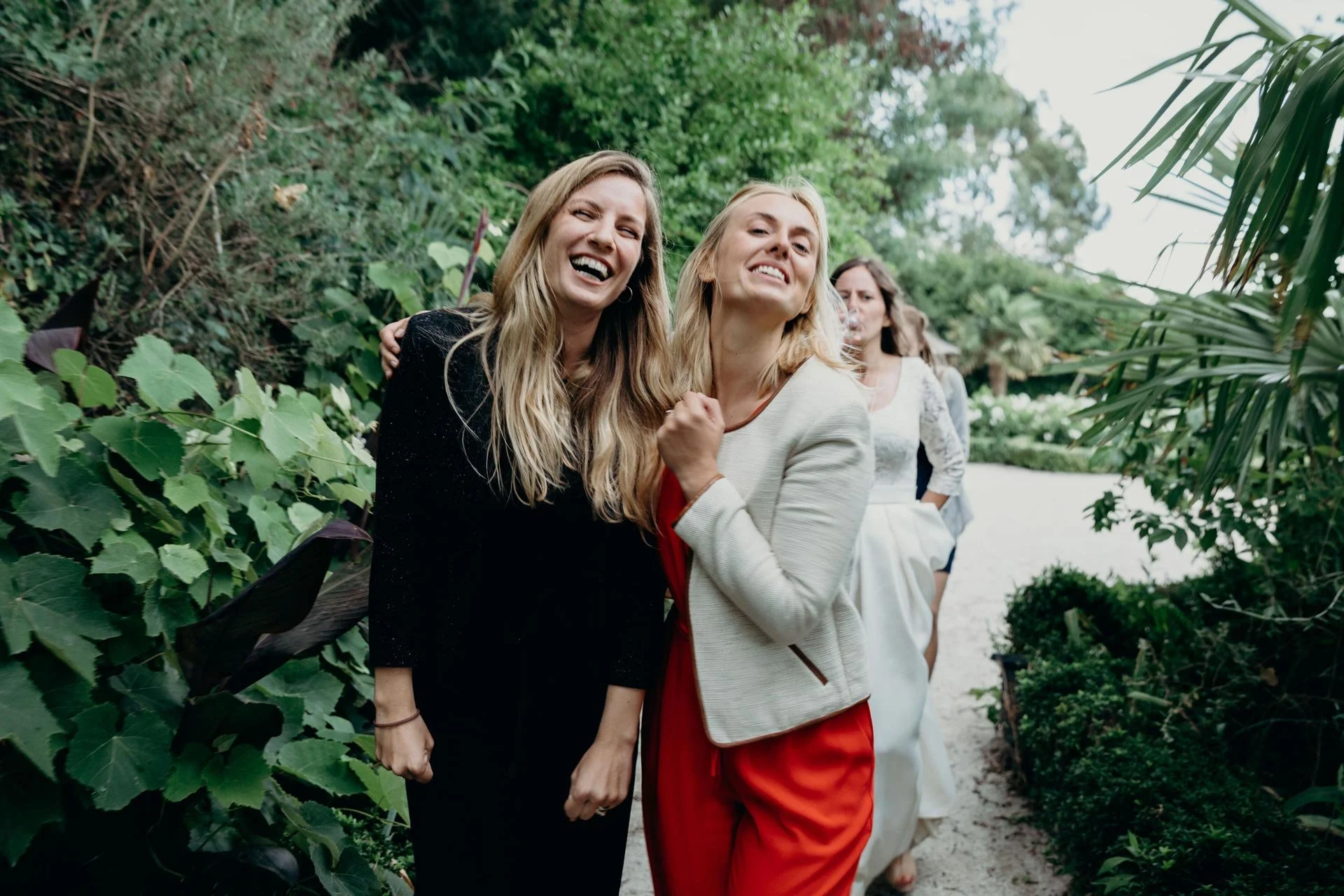 Photographe de reportage mariage, groupe de femmes souriantes marchant dans un jardin luxuriant en Normandie