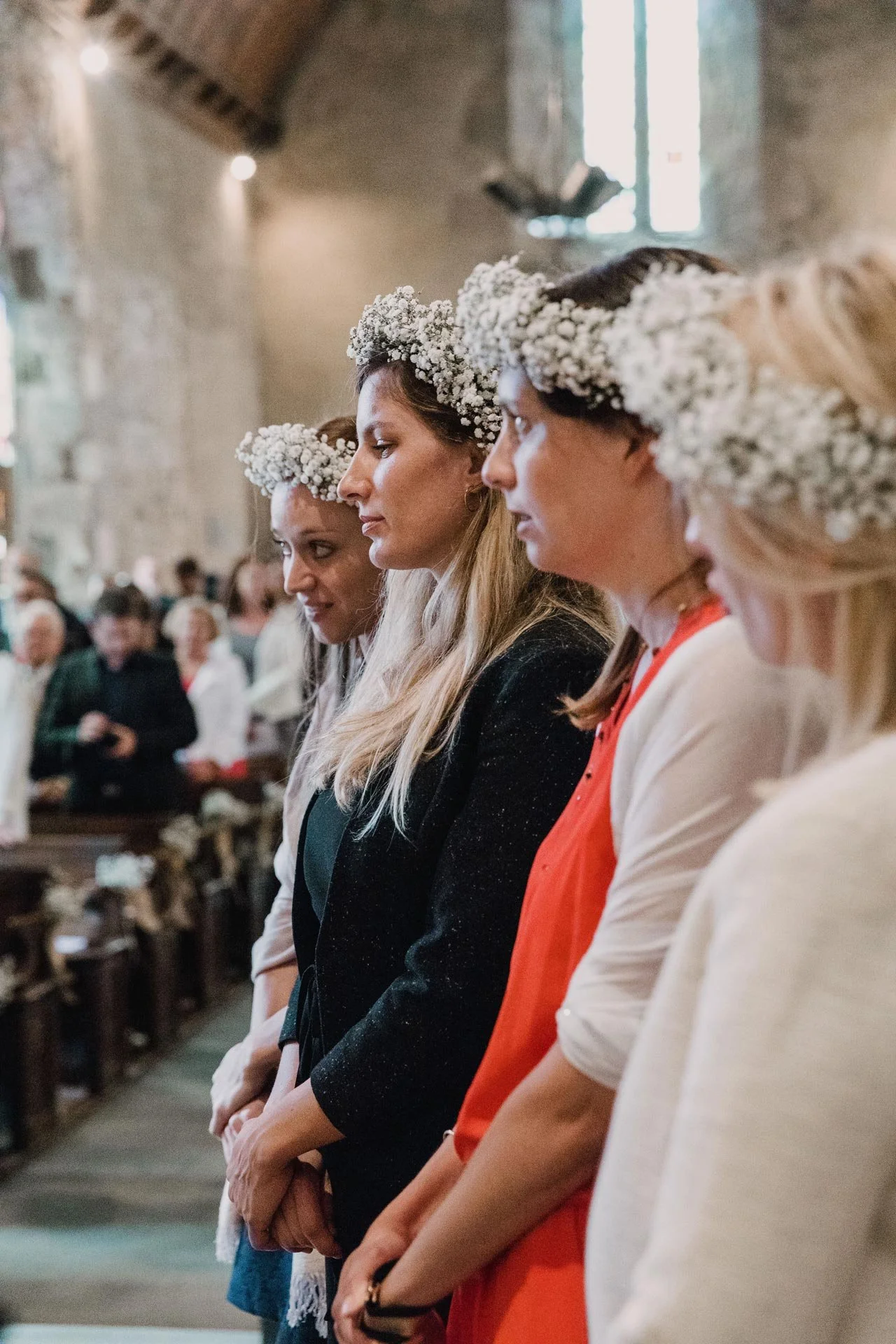 Photographe de mariage en Normandie, quatre femmes portant des couronnes de fleurs blanches assistent à une cérémonie religieuse