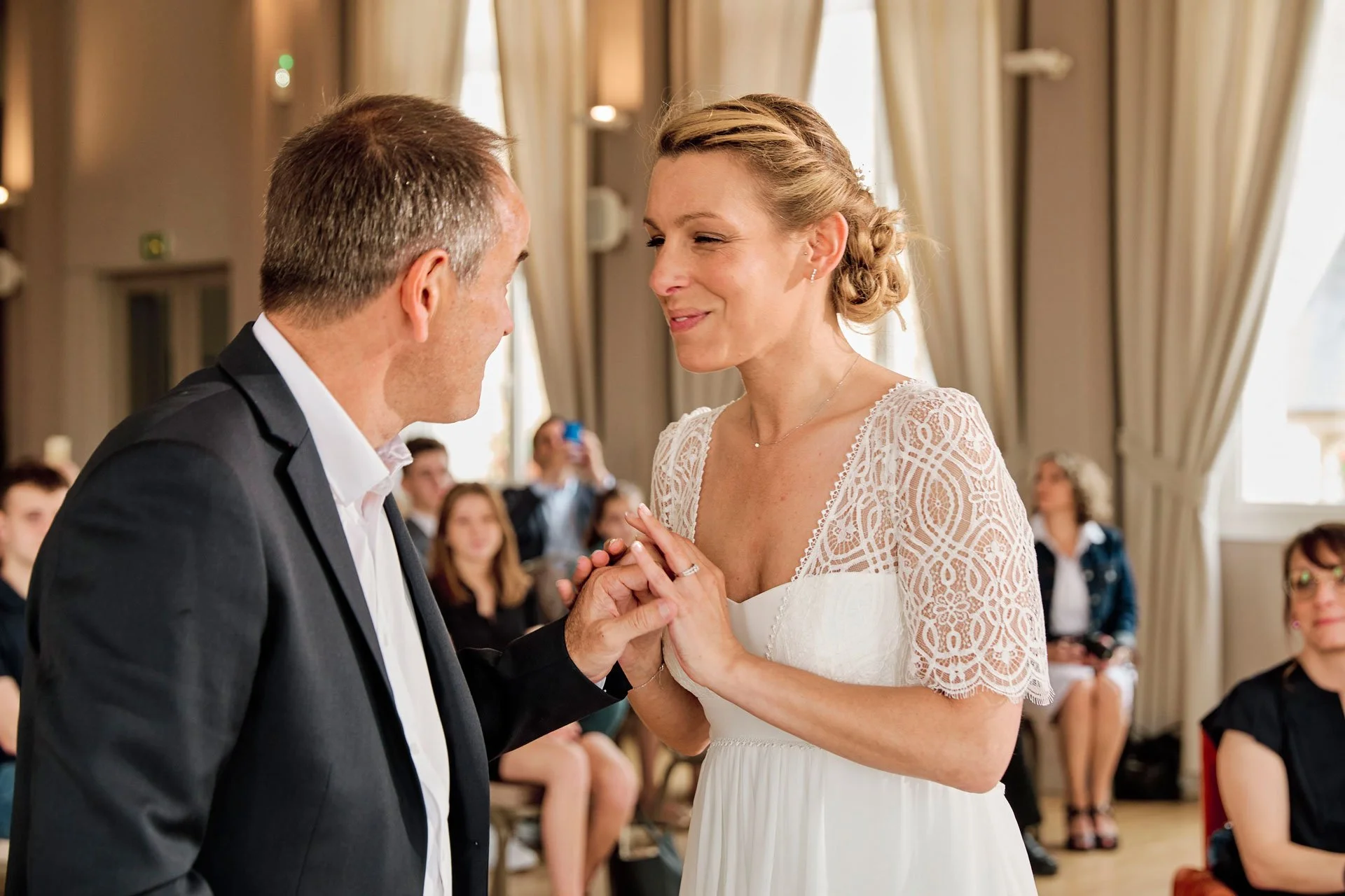 Une femme en robe de mariée tenant la main de son mari en costume lors d’une cérémonie civile à la mairie.