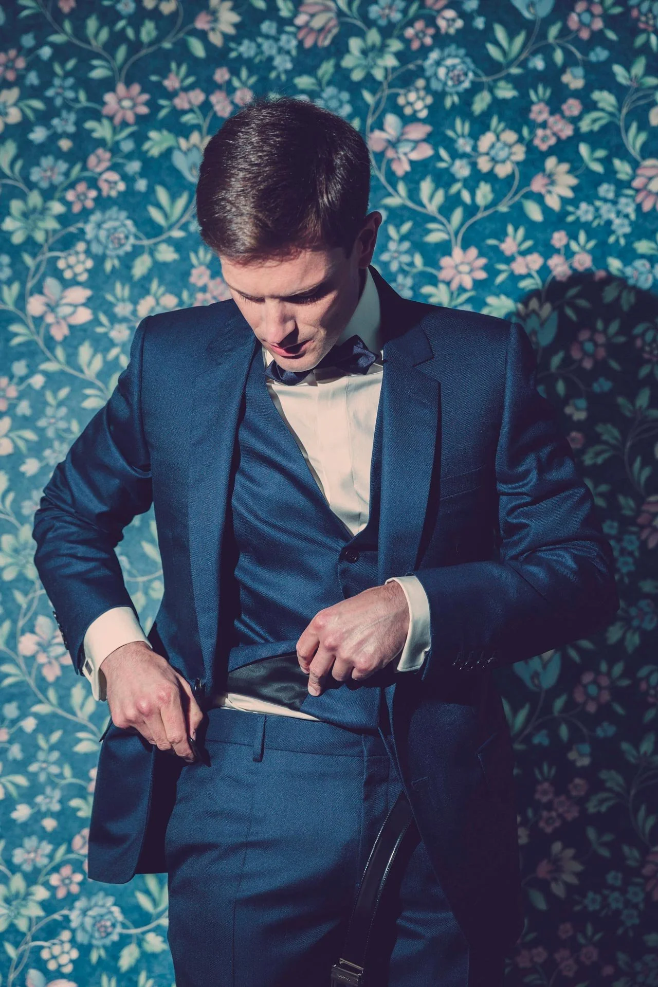 Marié en costume bleu devant un papier peint fleuri, portrait de mariage élégant