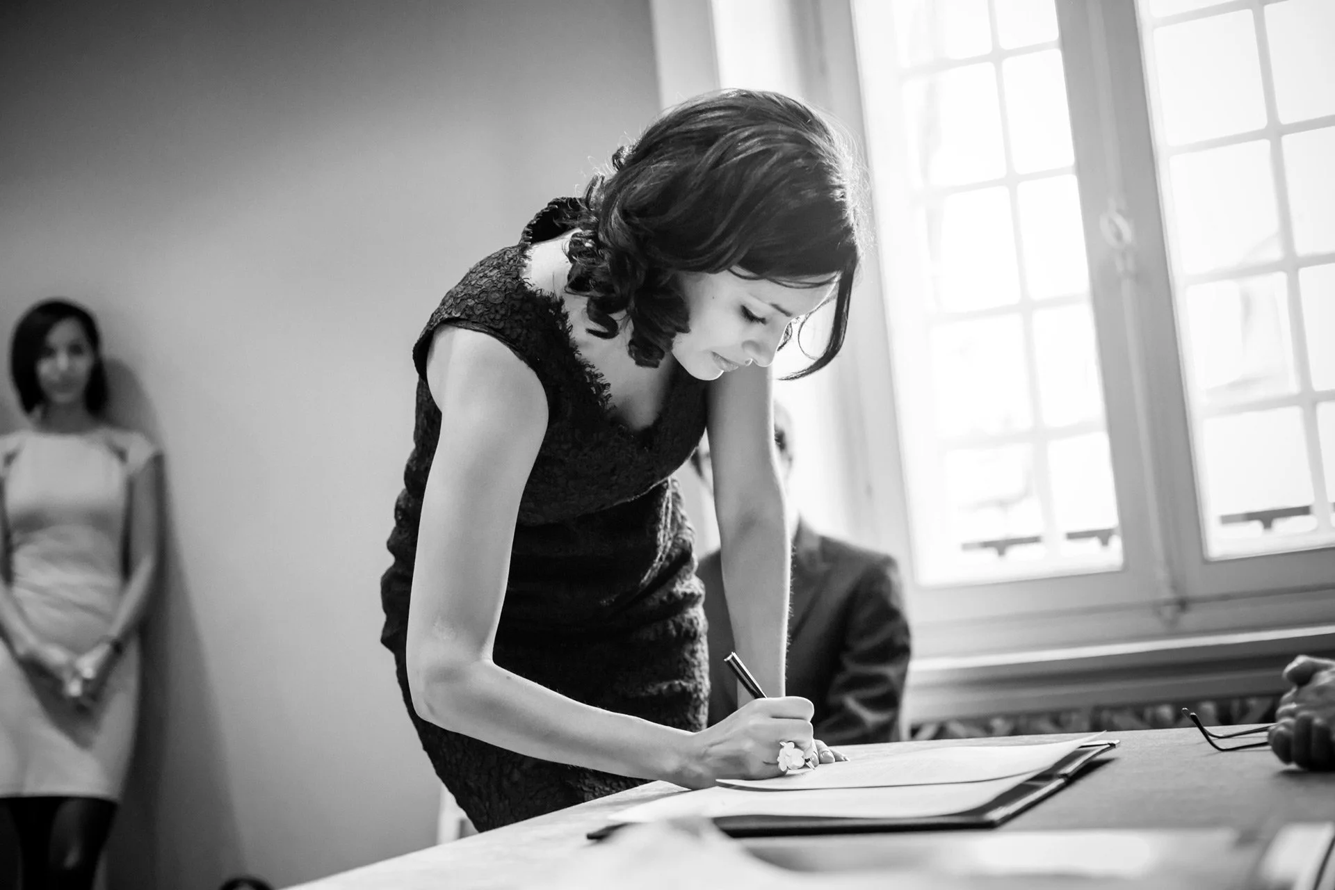 Femme témoin de mariage en robe noire signant un document lors d'une cérémonie.