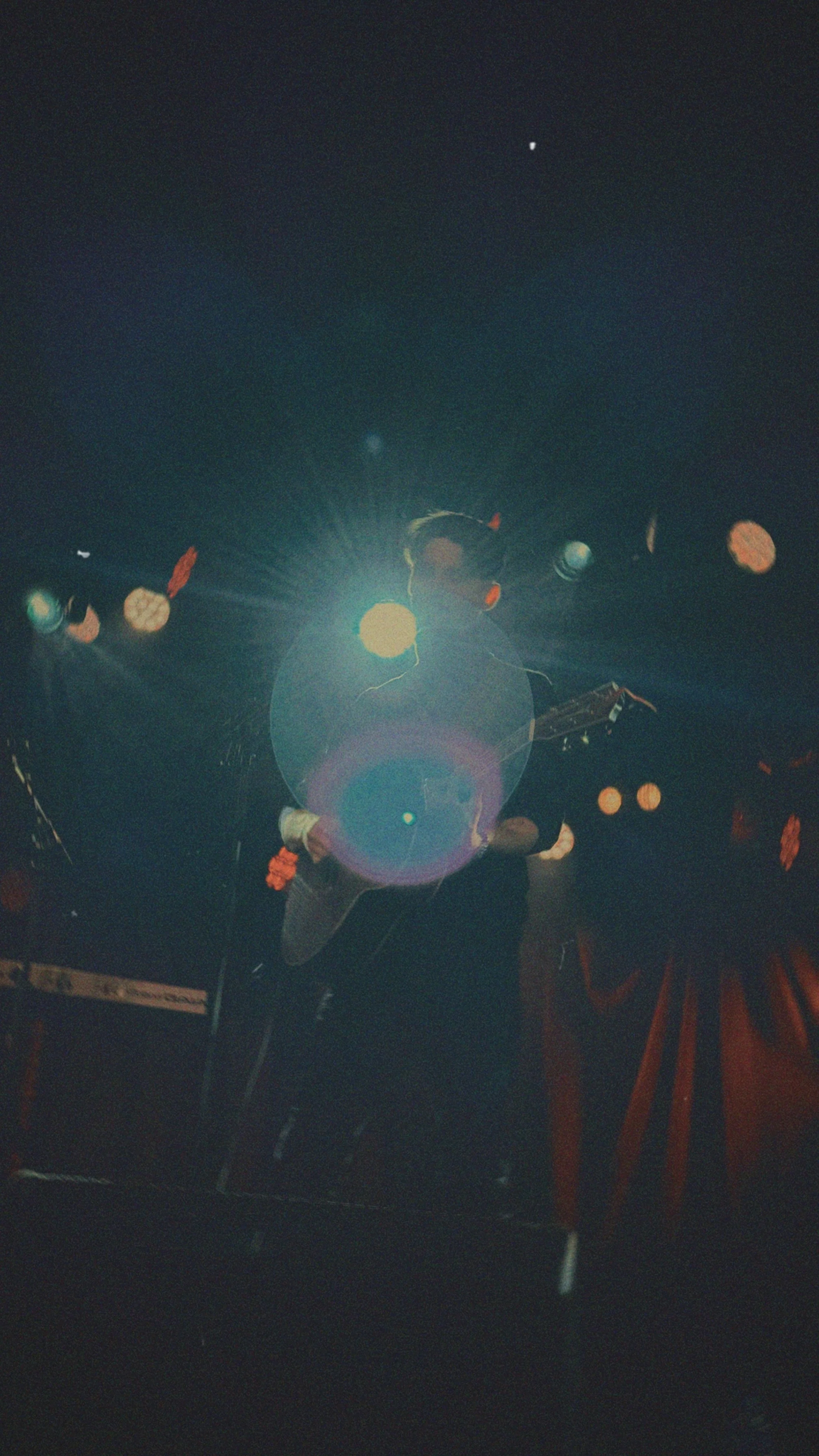Person with a guitar performing on stage under bright spotlight, with stage lights hanging above.