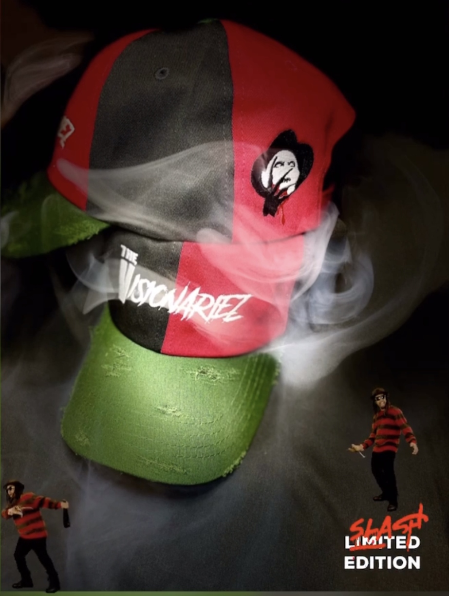 A cap with a red, black, and gray design featuring a stylized face and the words "The Visionariez." The cap has a green bill and is surrounded by wisps of smoke.