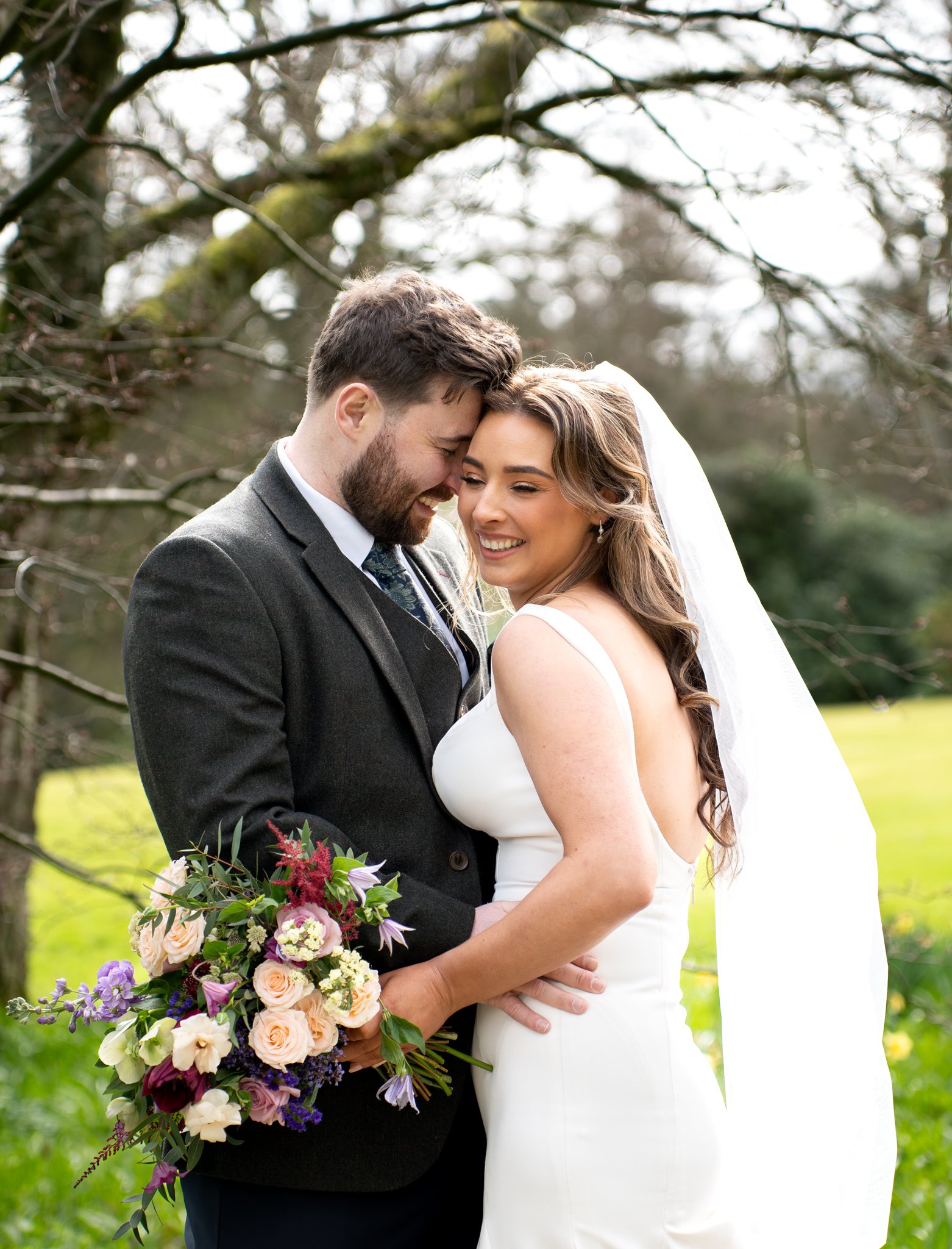 Bride and groom sharing a kiss outdoors during wedding, woman holding a colorful bouquet of flowers.