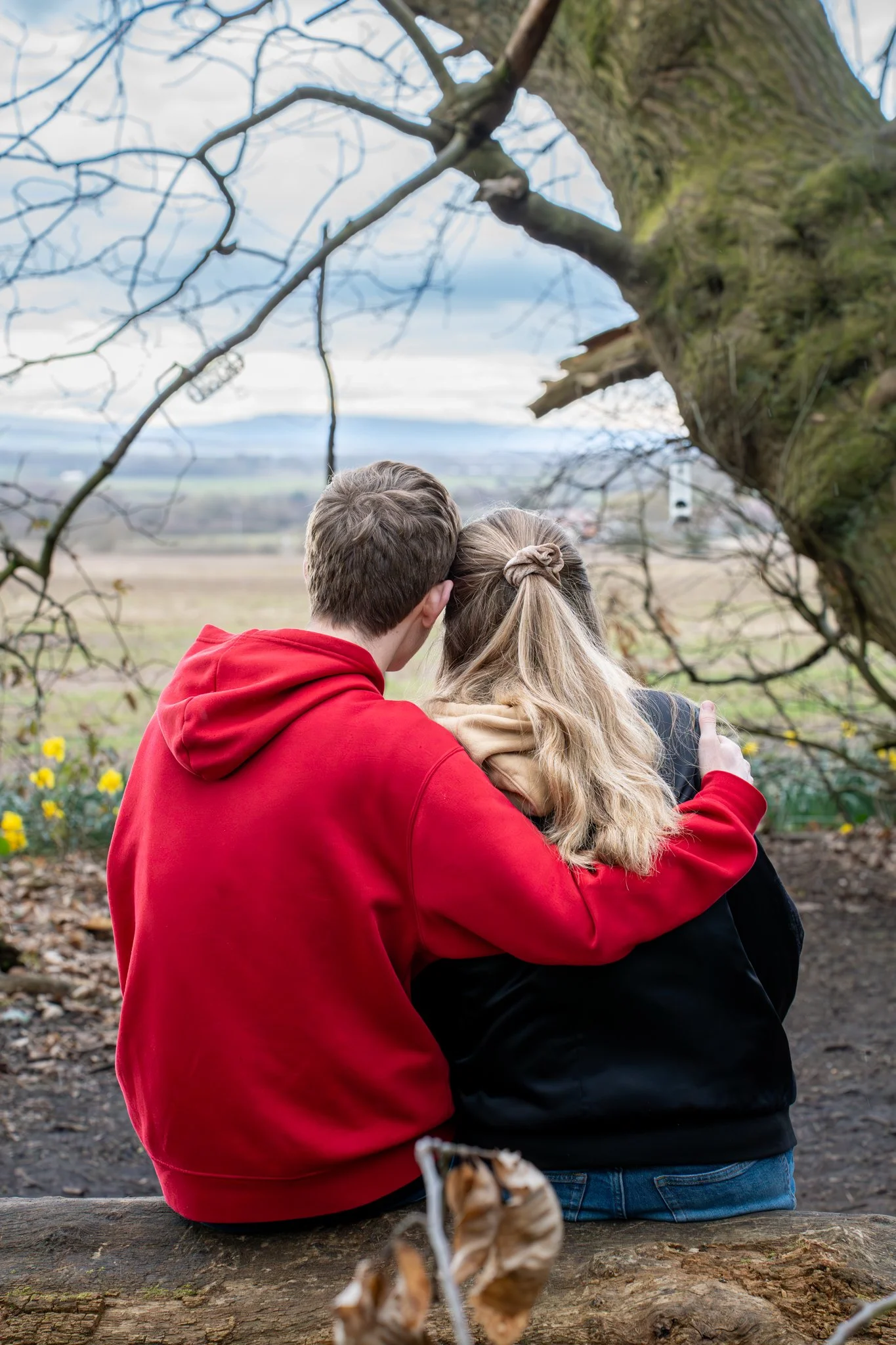 Close-up of two people hugging, focusing on their hands and arms, with one person wearing a black jacket and the other wearing a red sweatshirt.