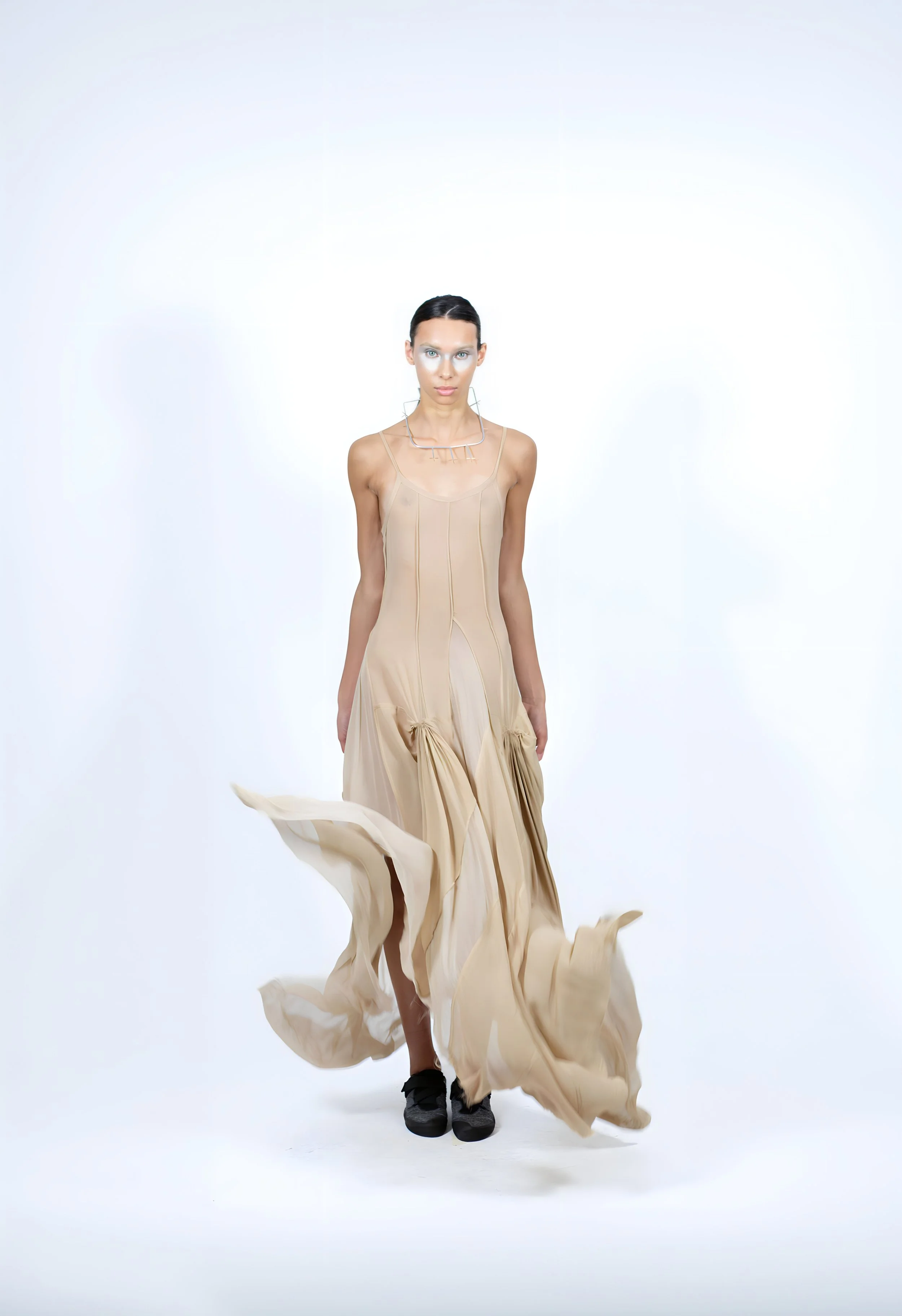 Une femme portant une robe longue beige en mouvement, sur fond blanc.